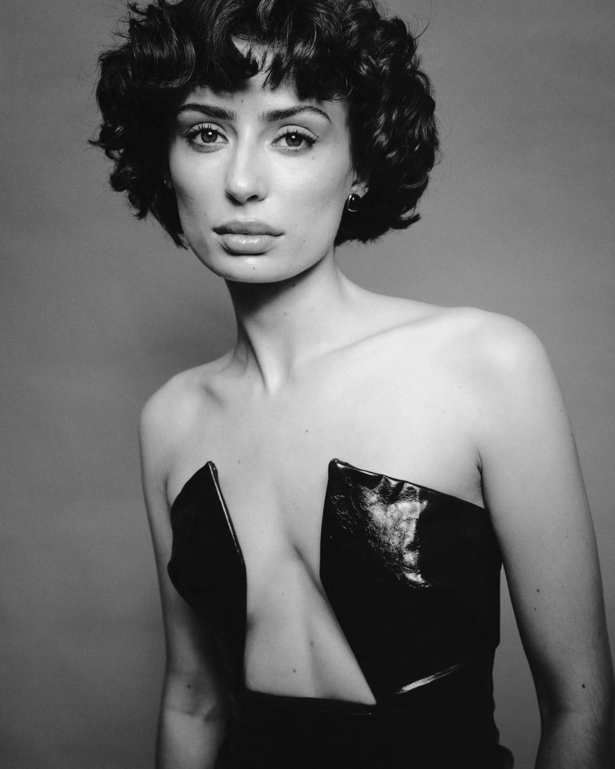 Black and white photo of a woman with short, curly hair wearing a strapless, shiny black dress.