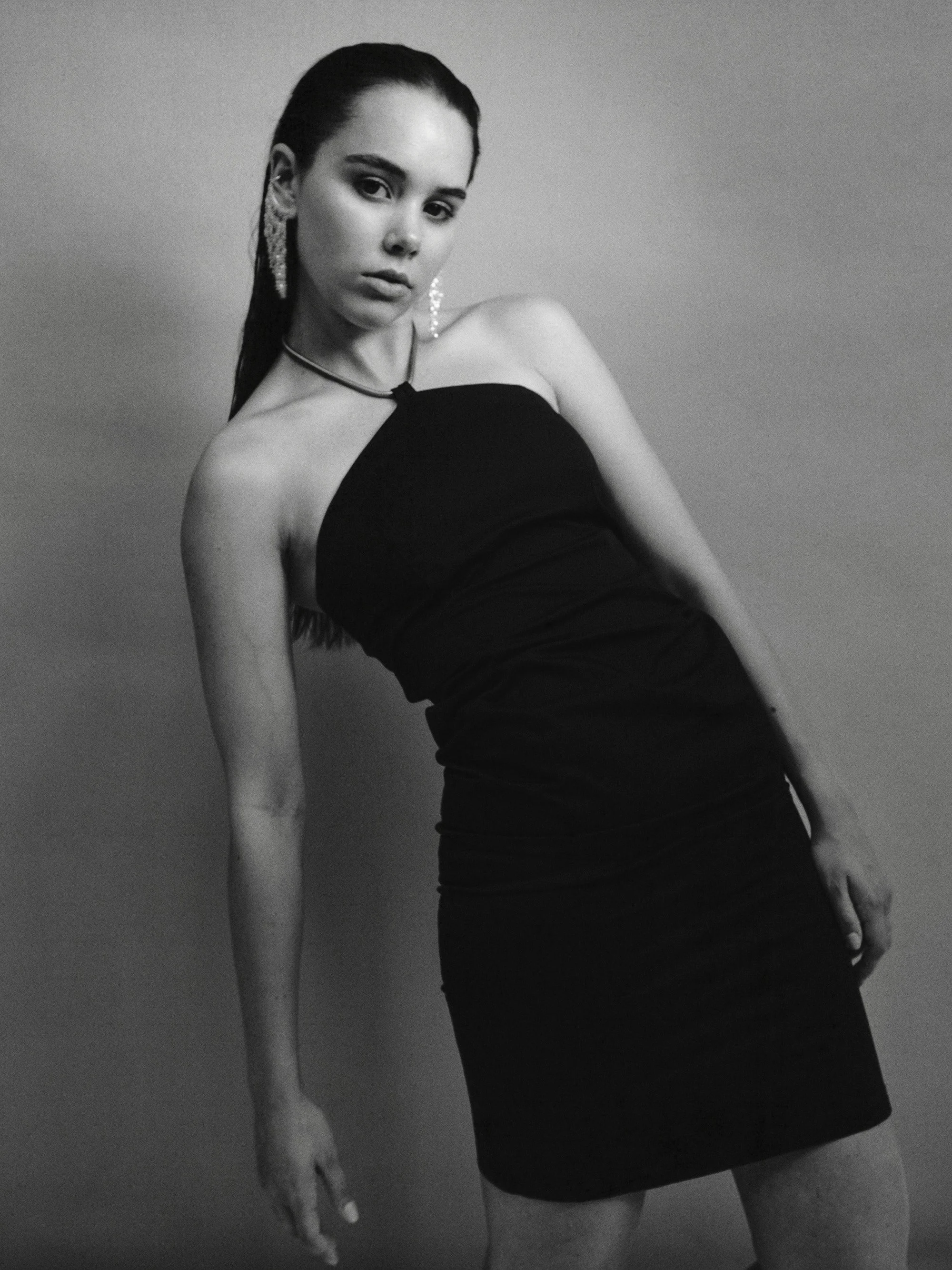 Black and white photo of a woman with long dark hair wearing a strapless black dress and earrings.