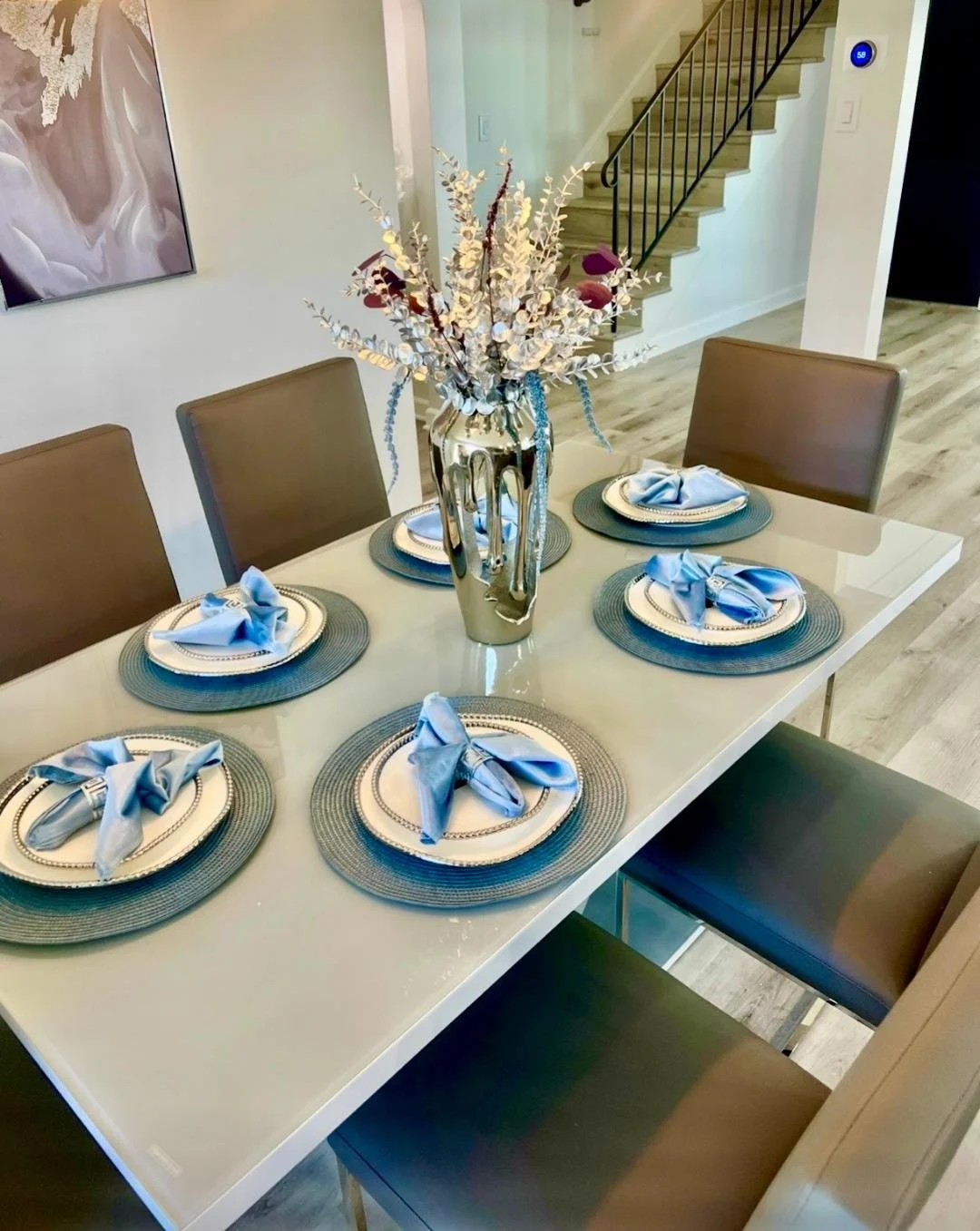 "Dining table styled with layered textures, timeless place settings, blue and chrome accents, create luxurious and inviting dining experiences."