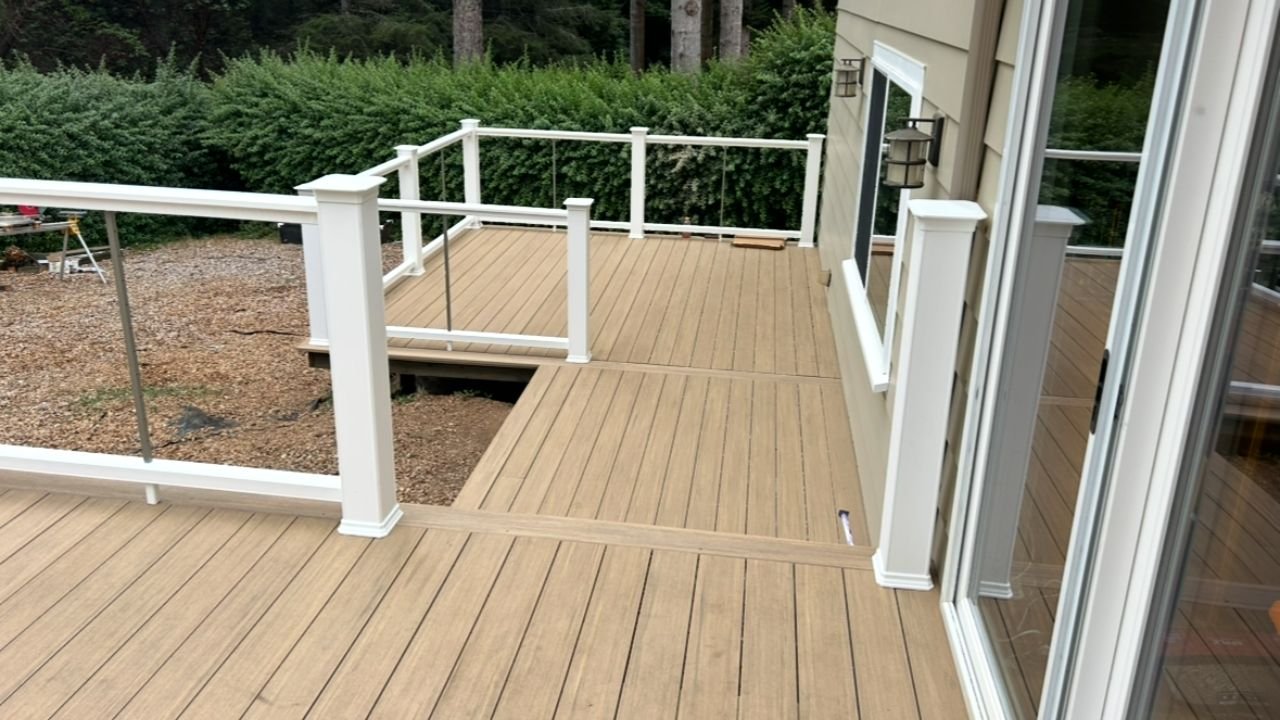 Empty wooden deck with white railing attached to a house, overlooking a backyard with bushes and trees.