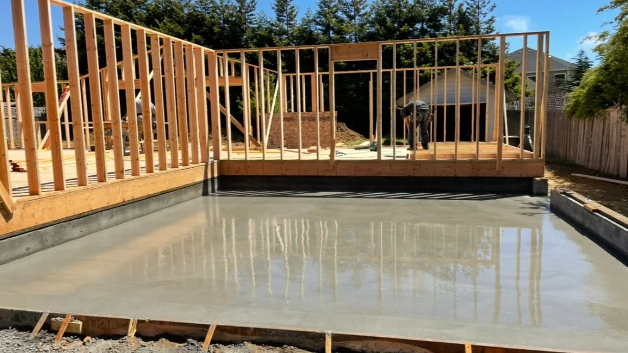 Construction site with wooden framing for a building, concrete slab on the ground, and workers in the background during daytime