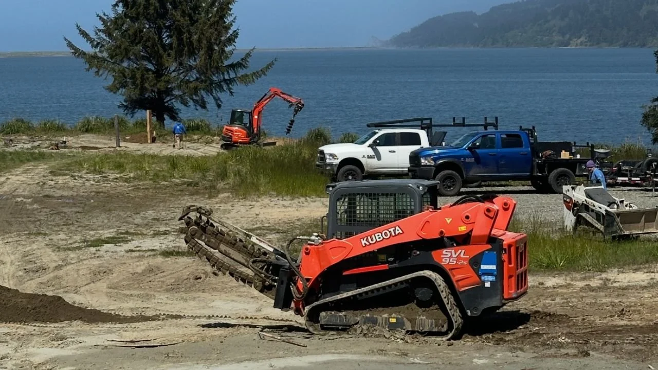 Construction site near a body of water with a mini excavator and trucks