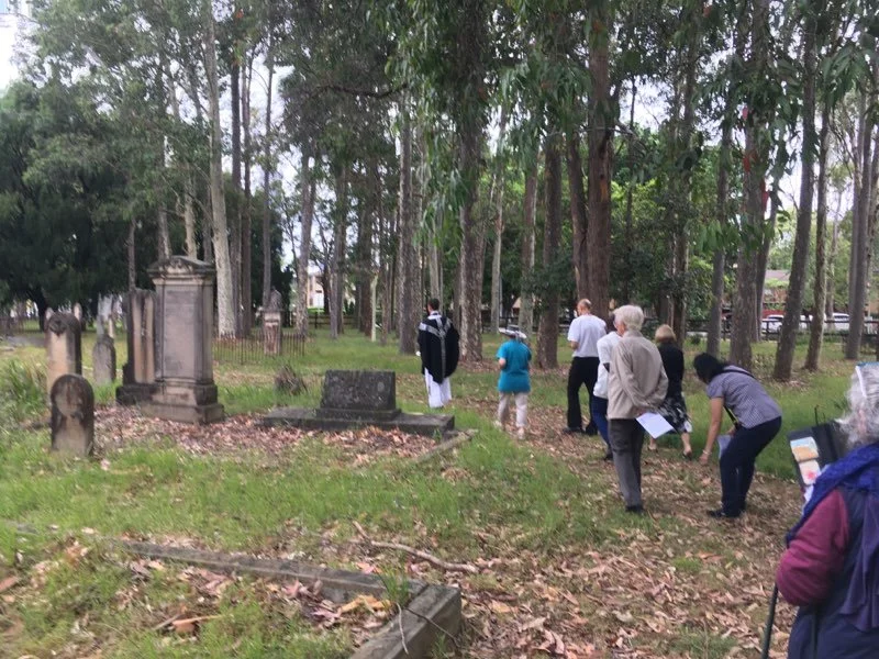 Group of people walking through a cemetery with old headstones and trees.