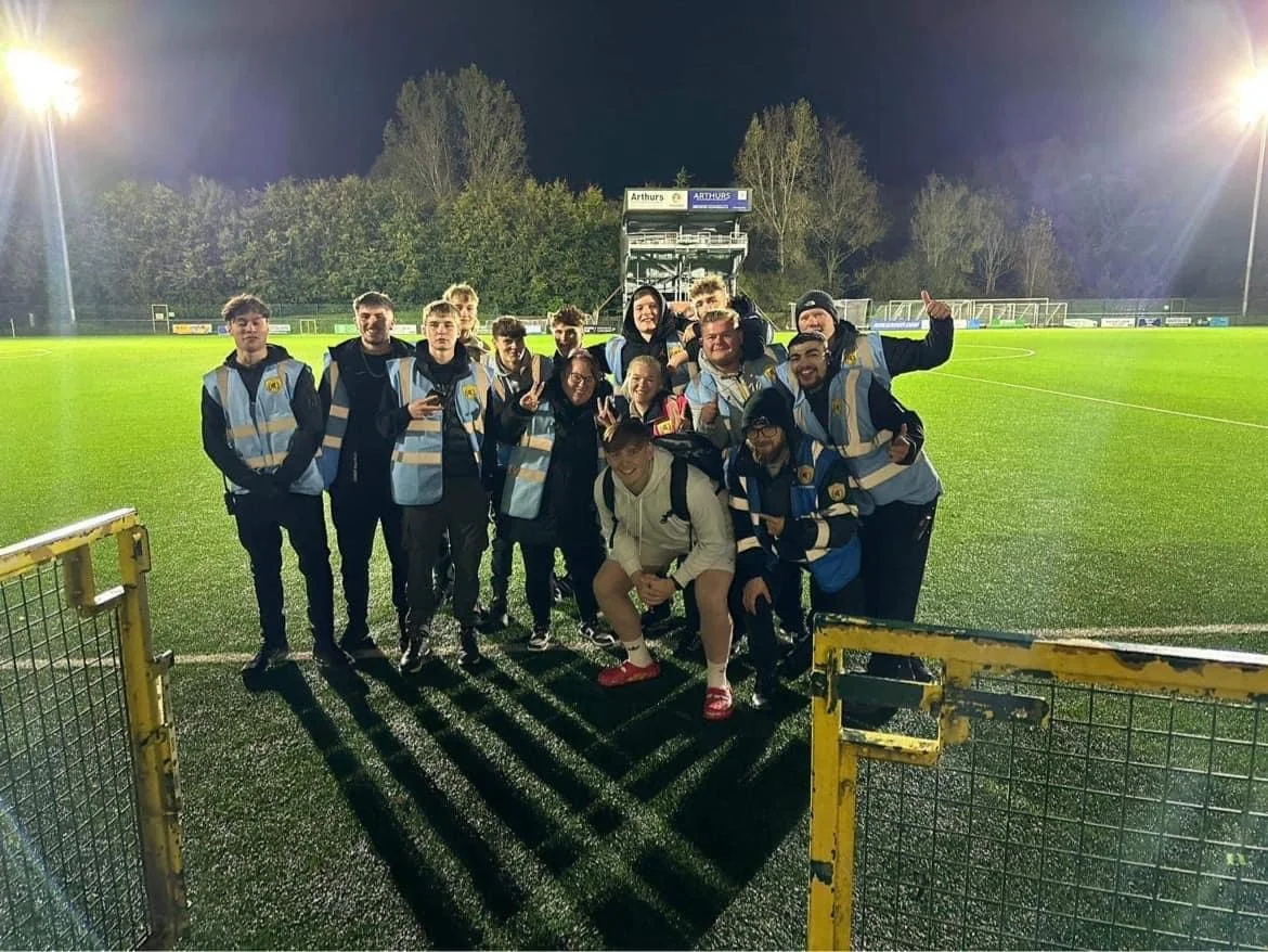 Group of young soccer players and coaches on a well-lit outdoor soccer field at night, posing for a photo.