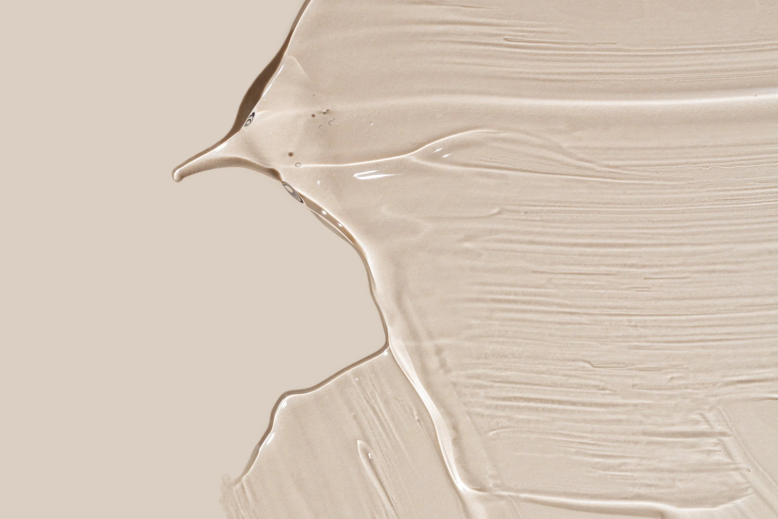 Beige cream foundation streaked with visible brush strokes with a portion of thicker liquid cream in the upper left corner.