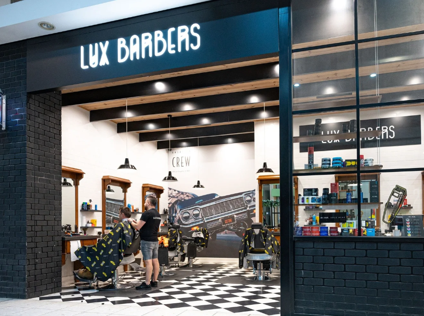 Interior of Lux Barbers with barbershops, customers, and barber chairs, decorated in black and white with a large car mural on the wall.
