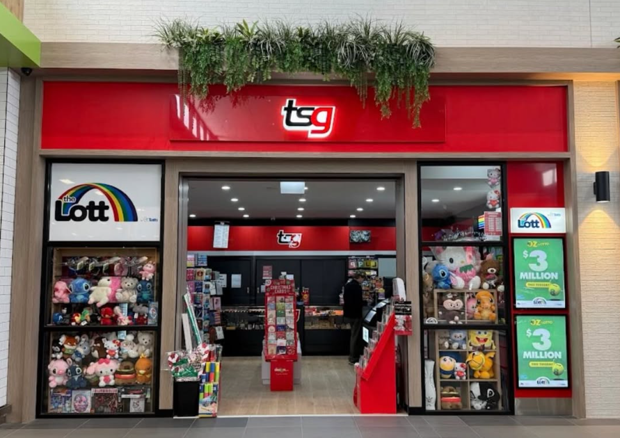 Exterior view of a toy and lottery store named 'TSG' with plush toys displayed in glass cases on either side of the entrance, and promotional lottery signs on the right.