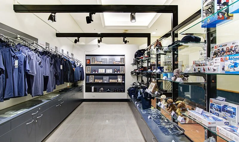 Police merchandise store with police uniforms on the left, police hats and toys on display on the right, and a shelf with awards and souvenirs at the back.