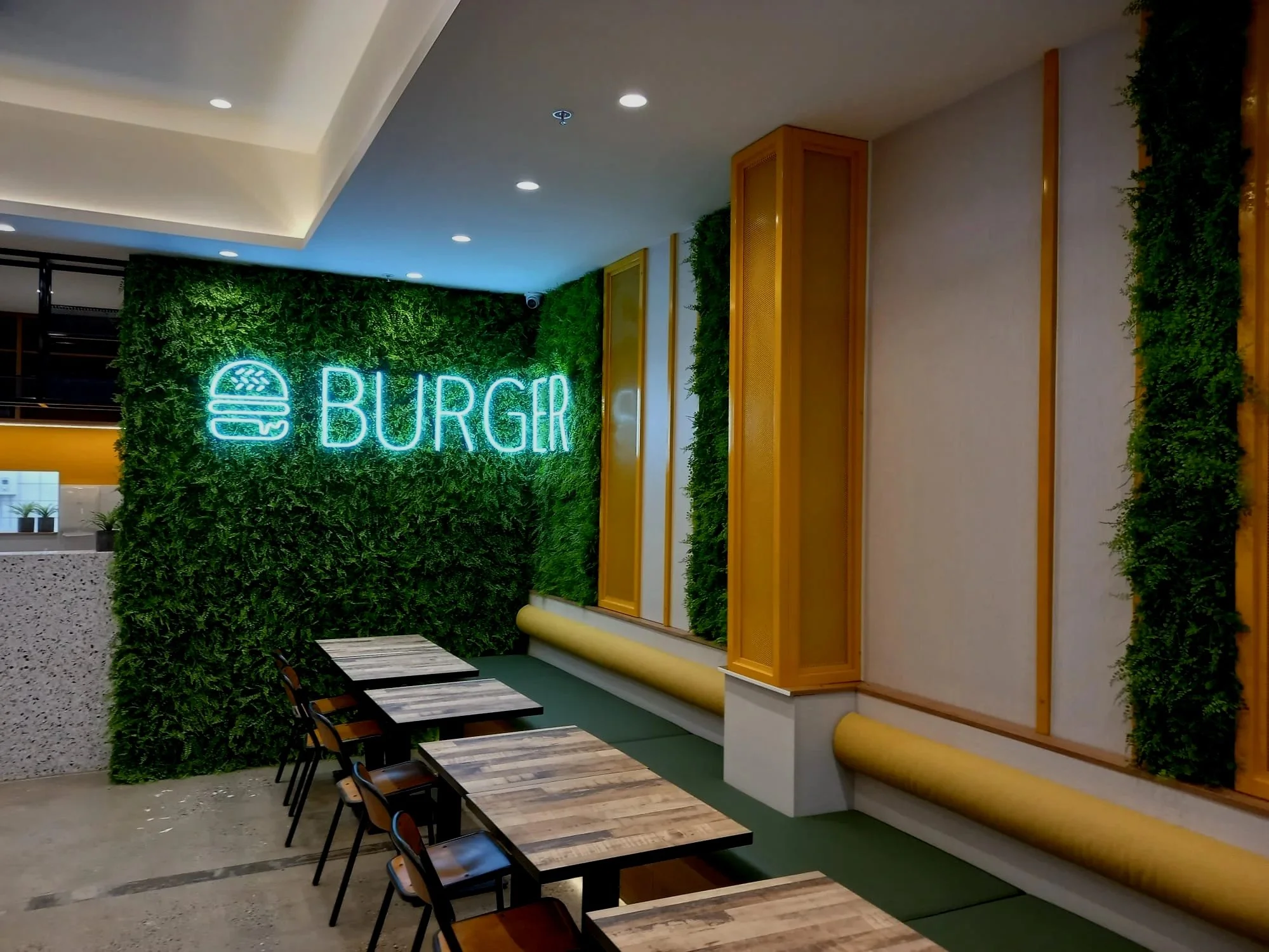 Interior of a burger restaurant with a green wall and neon sign reading 'BURGER' next to a burger icon.