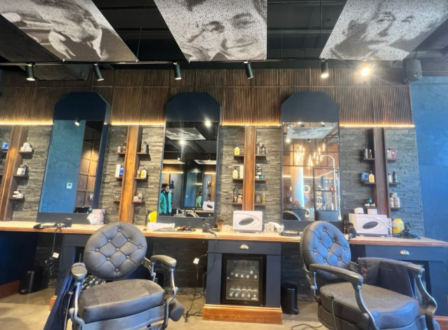 Barber chairs in front of a mirror with shelves and decor in a modern salon interior.