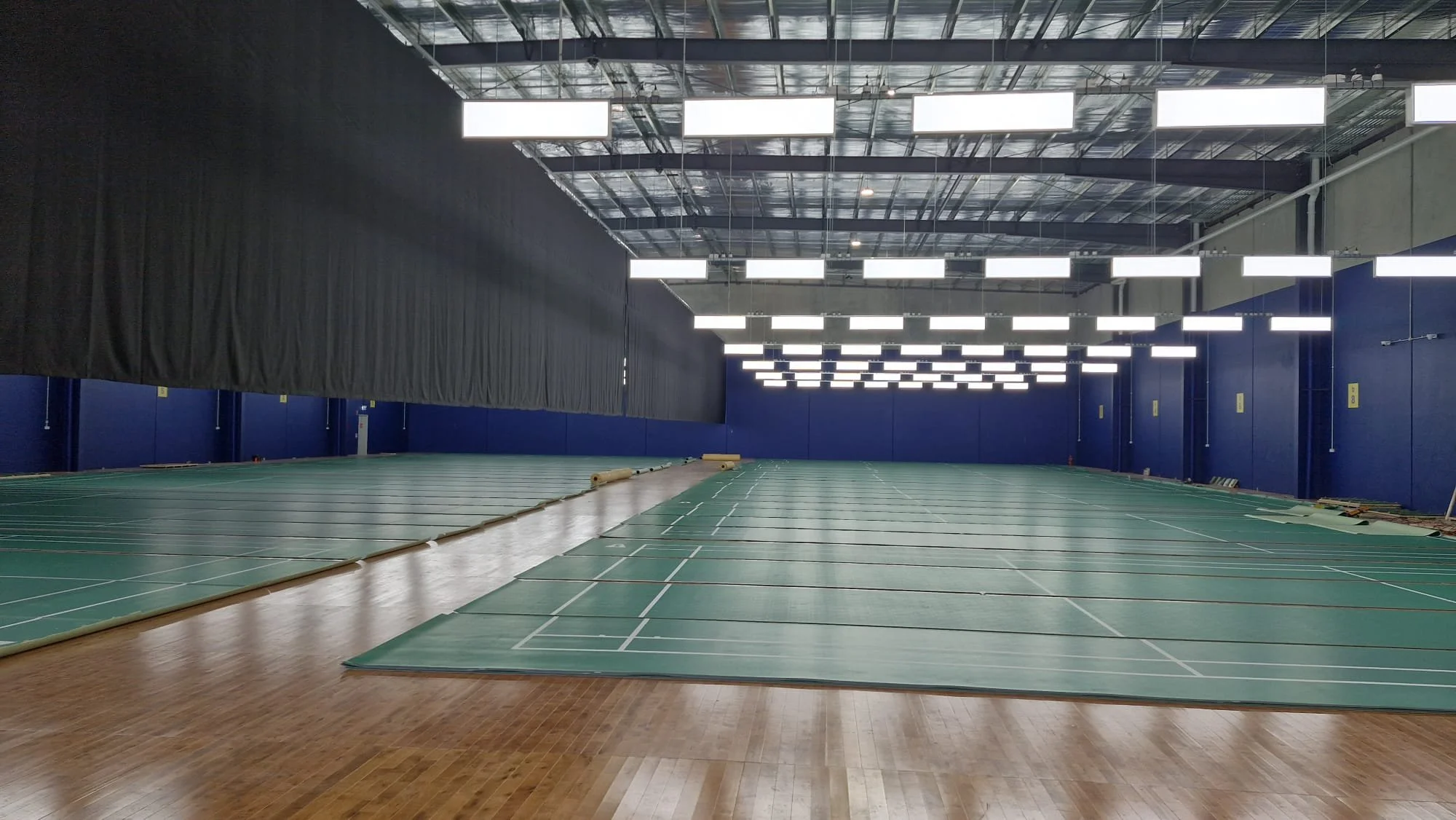 Empty indoor sports facility with green mats on the floor and bright overhead lights.