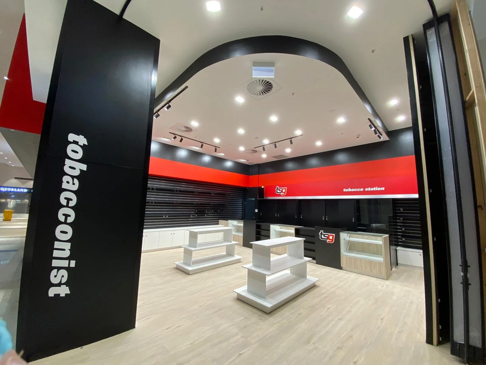 Empty tobacco shop with black, red, and white decor, shelves, and display cases, and a sign reading 'tobacco station' on the wall.