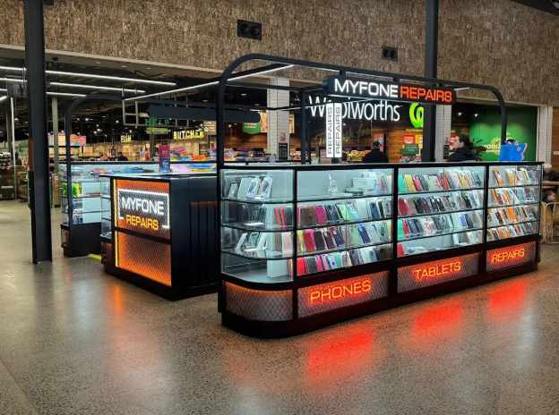 Mobile phone accessories kiosk in a shopping mall with signs for 'Phones,' 'Tablets,' and 'Repairs'.