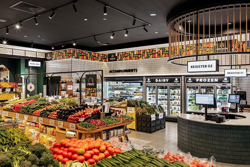 Interior of a grocery store produce section with fresh vegetables and dairy products, registers, and colorful decor.