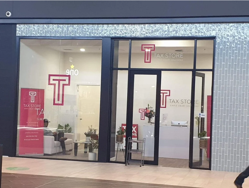 Exterior view of a tax store with glass windows and doors, displaying the store's logo and interior with chairs, plants, and a reception desk.