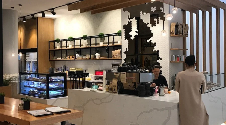 Coffee shop interior with counter, display case, barista, and customer.