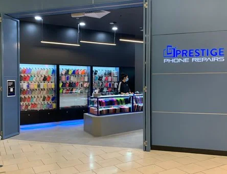 Inside a phone repair shop with a display of colorful phone cases on walls and a table with phone accessories. The shop has a sign that reads "Prestige Phone Repairs".