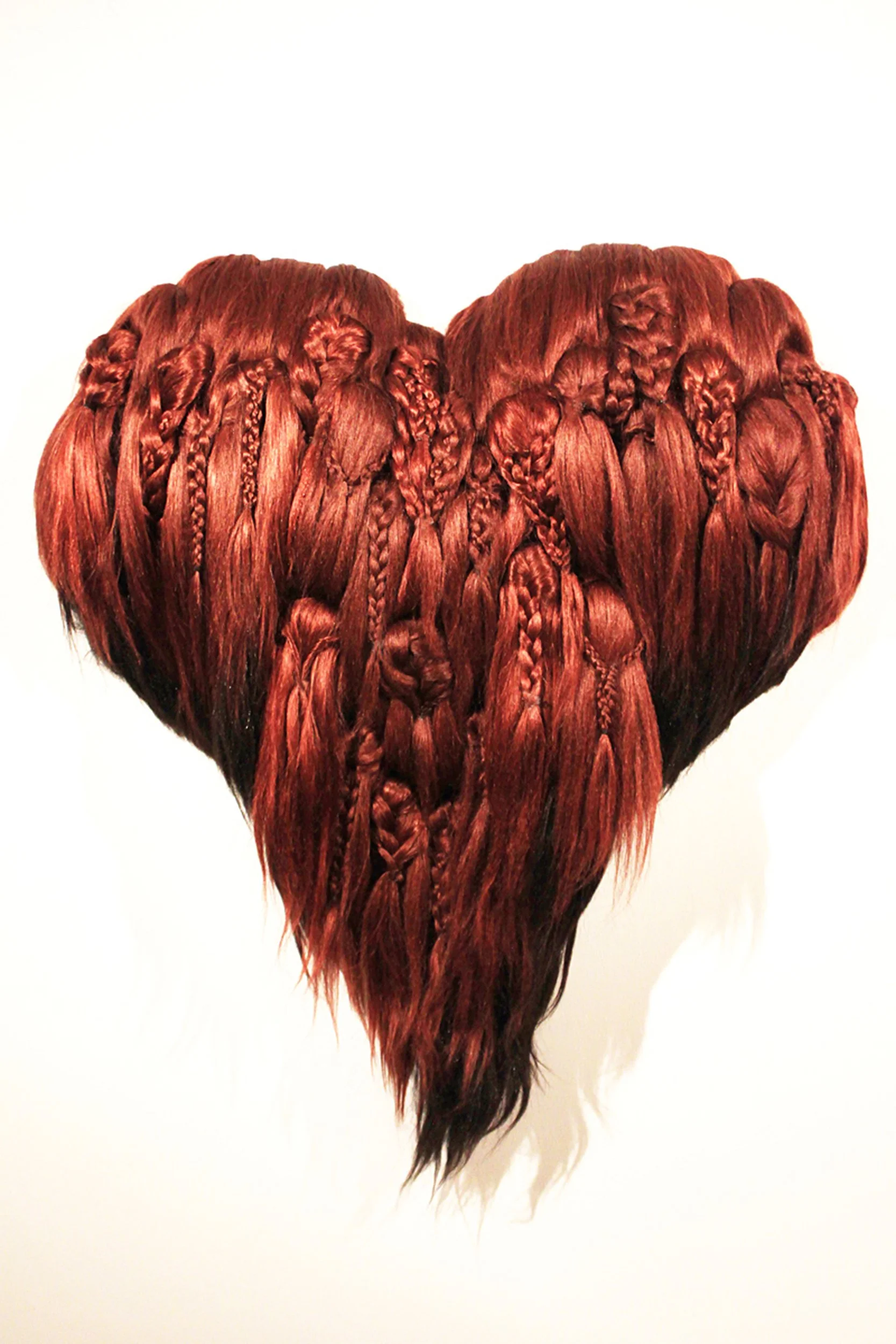 Close-up of a heart-shaped lock of red braided hair against a white background.