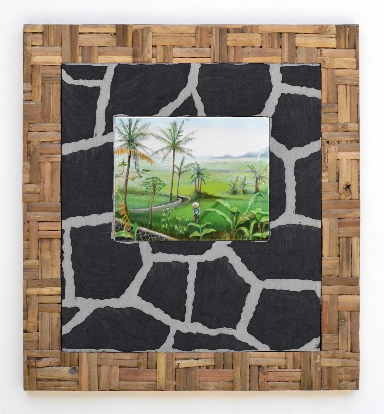 Painting of a lush green landscape with palm trees and a person wearing a hat, set on a wooden and black-and-white patterned background.