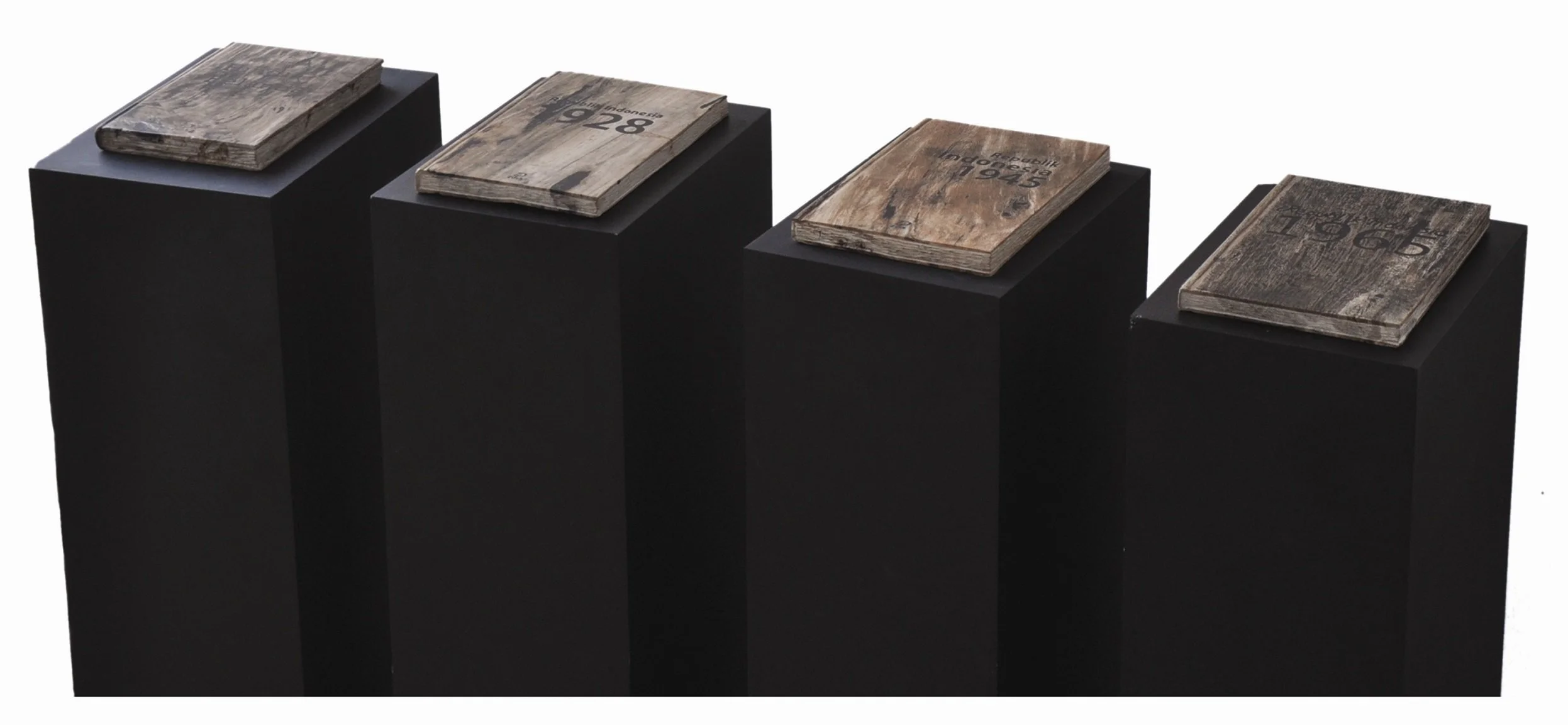 Four black pedestals, each displaying a weathered wooden book or booklet with various markings and text, against a plain white background.