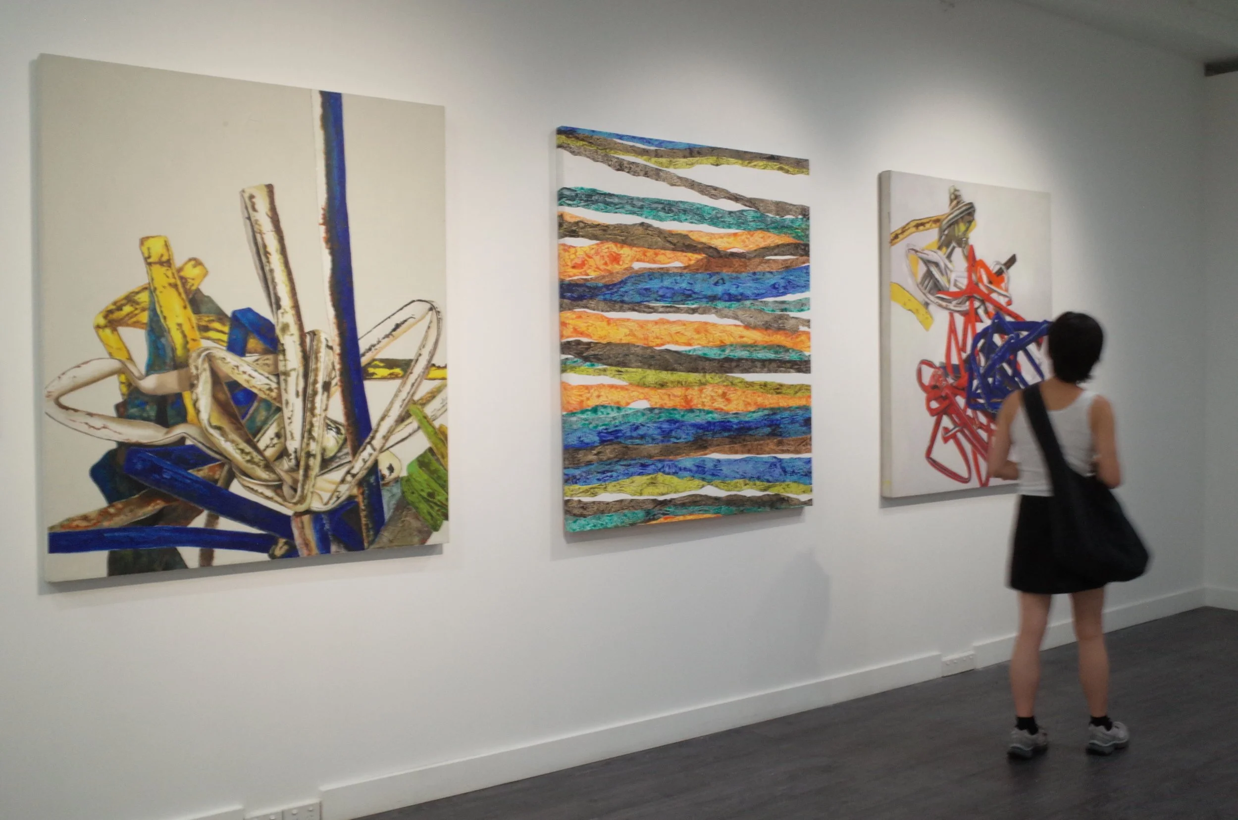 An art gallery wall displaying three abstract paintings, with a person walking past and observing the artwork.