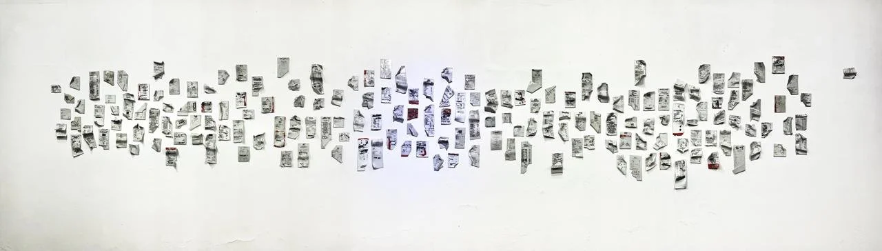 A wall covered with numerous small black-and-white pages or photos arranged in a scattered pattern.