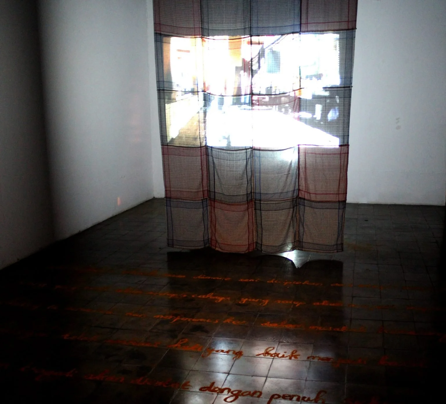Room with a window covered by a patterned curtain, sunlight outside, dark tiled floor with red text projected onto it.