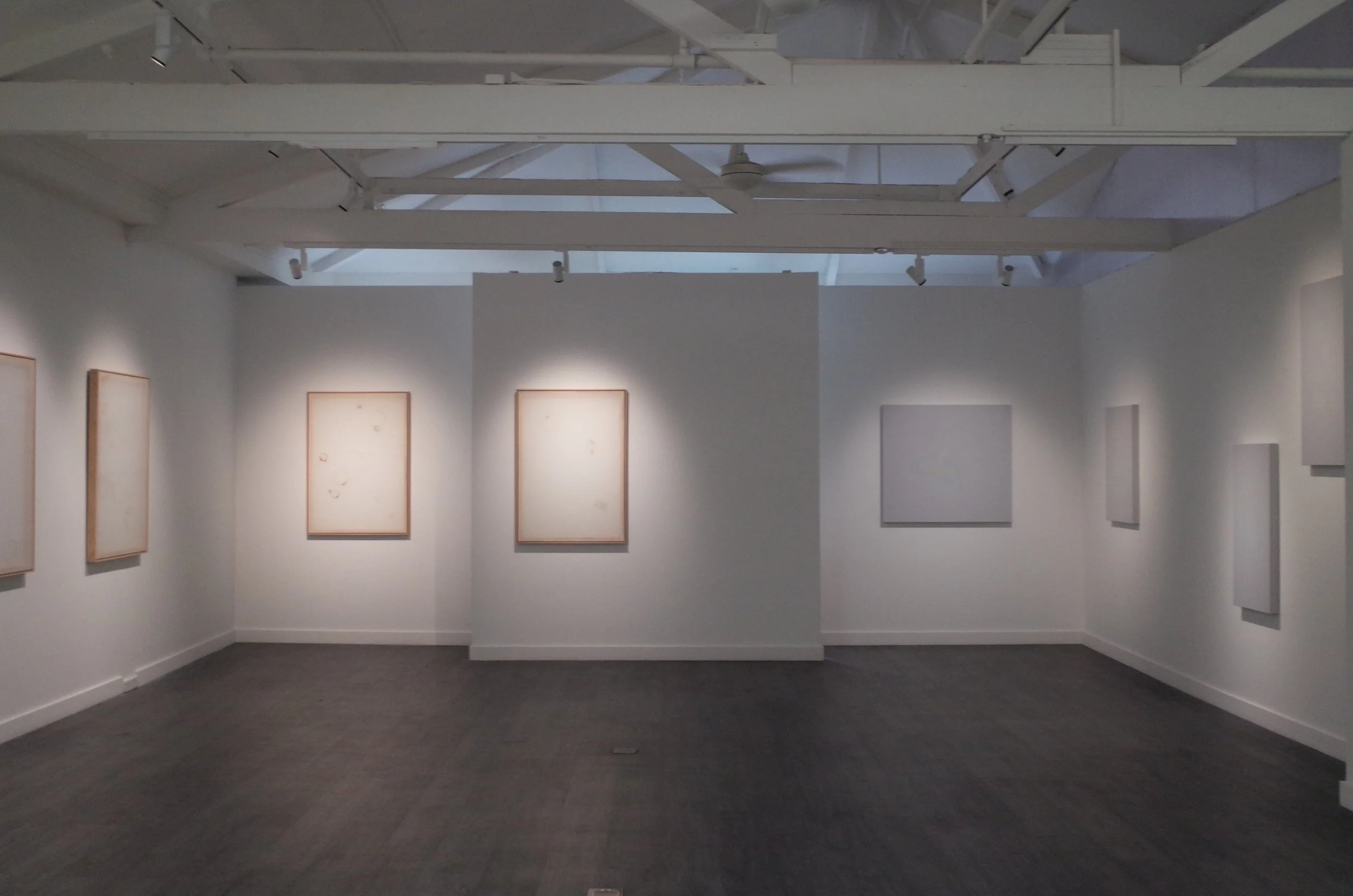An art gallery with white walls displaying framed art pieces, and a high ceiling with exposed beams and ventilation.