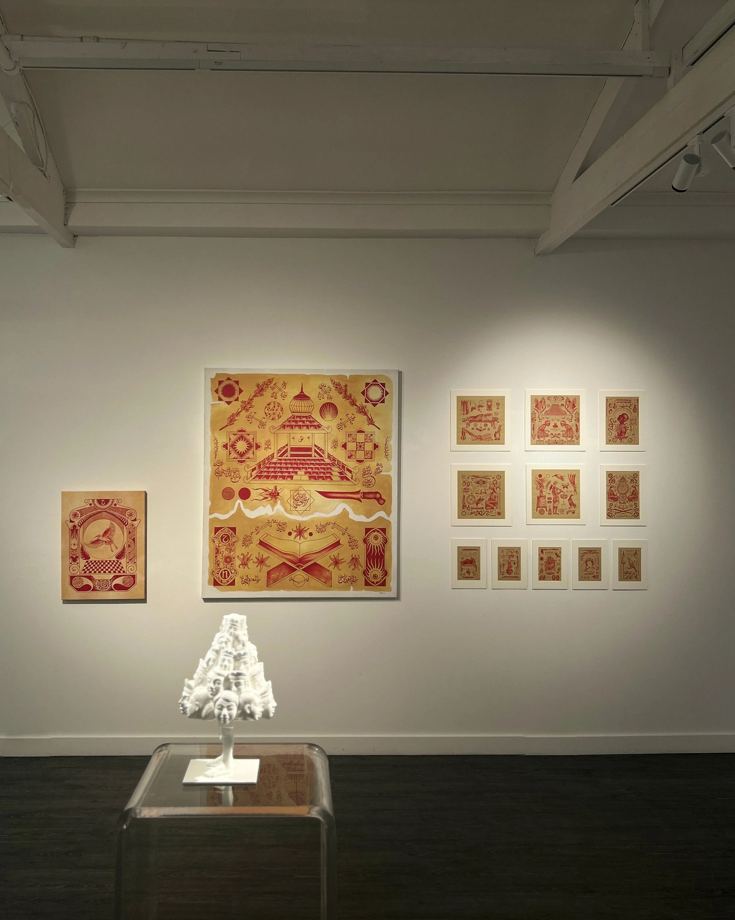 Art exhibit featuring red and gold prints on the wall and a white sculpture of faces on a display table.