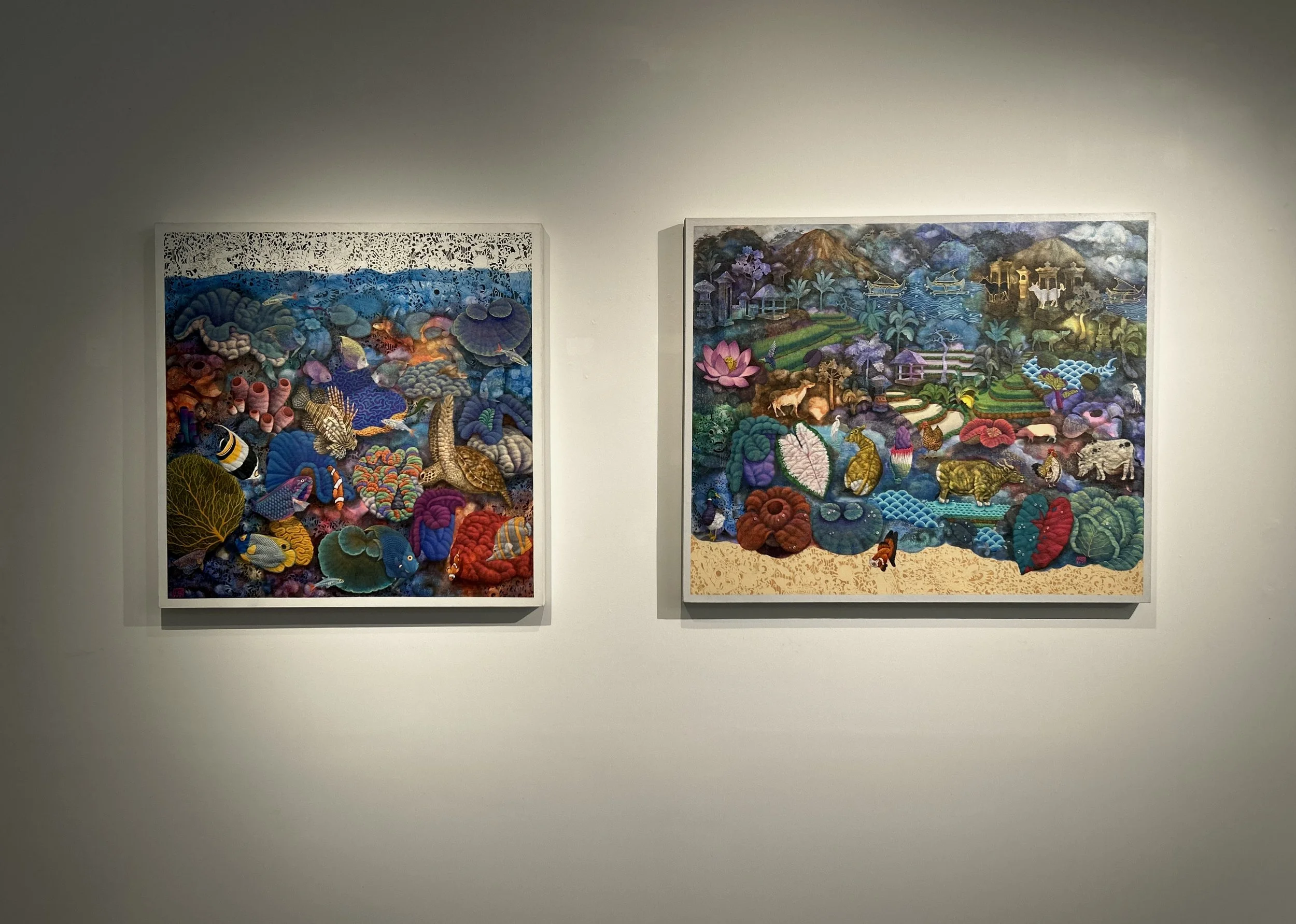 Two colorful textile art pieces on white wall, depicting vibrant underwater scenes with corals, fish, mountains, lakes, trees, animals, and landscapes.