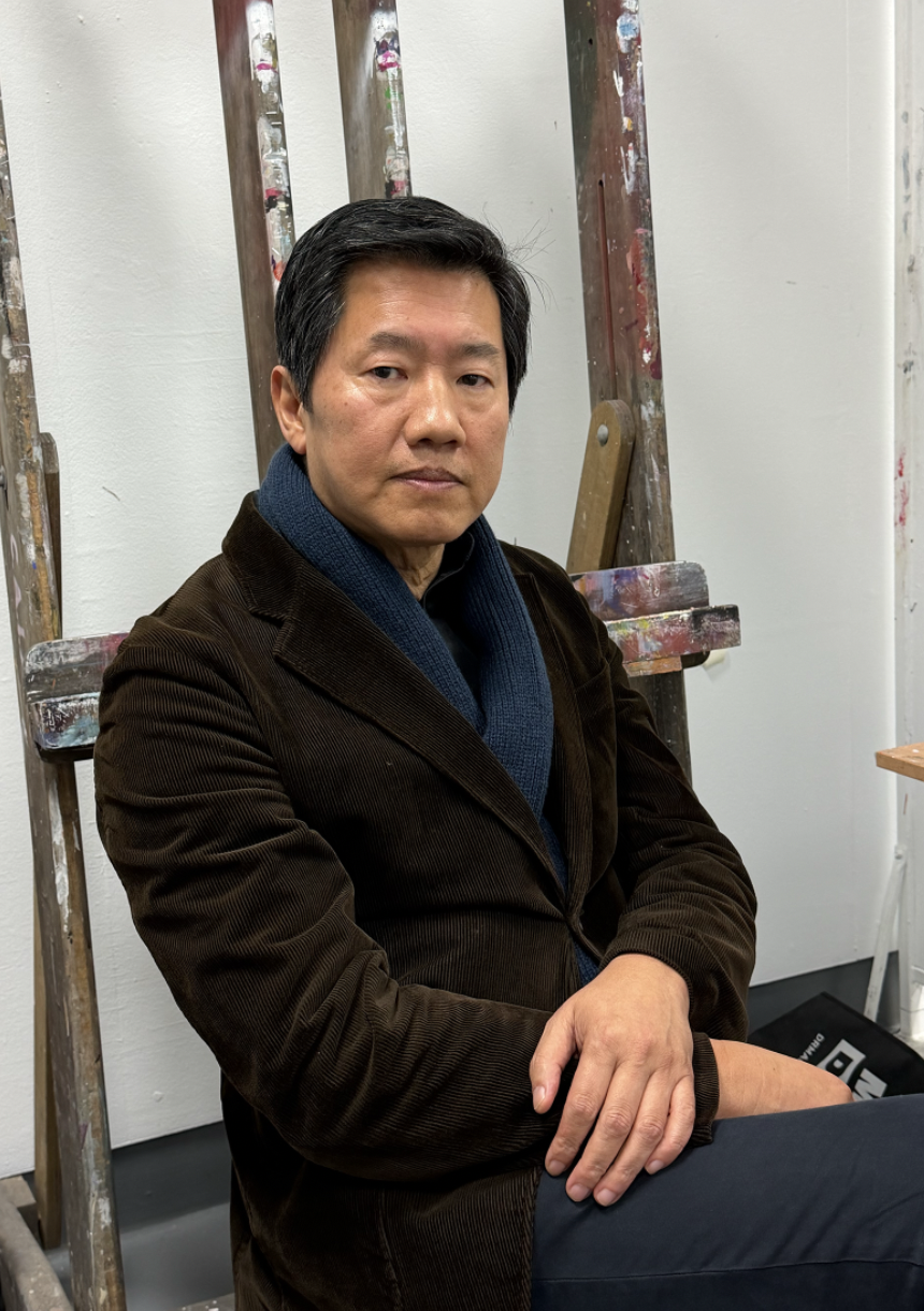 A man sitting in front of a metal ladder, wearing a brown corduroy jacket and a dark blue scarf.