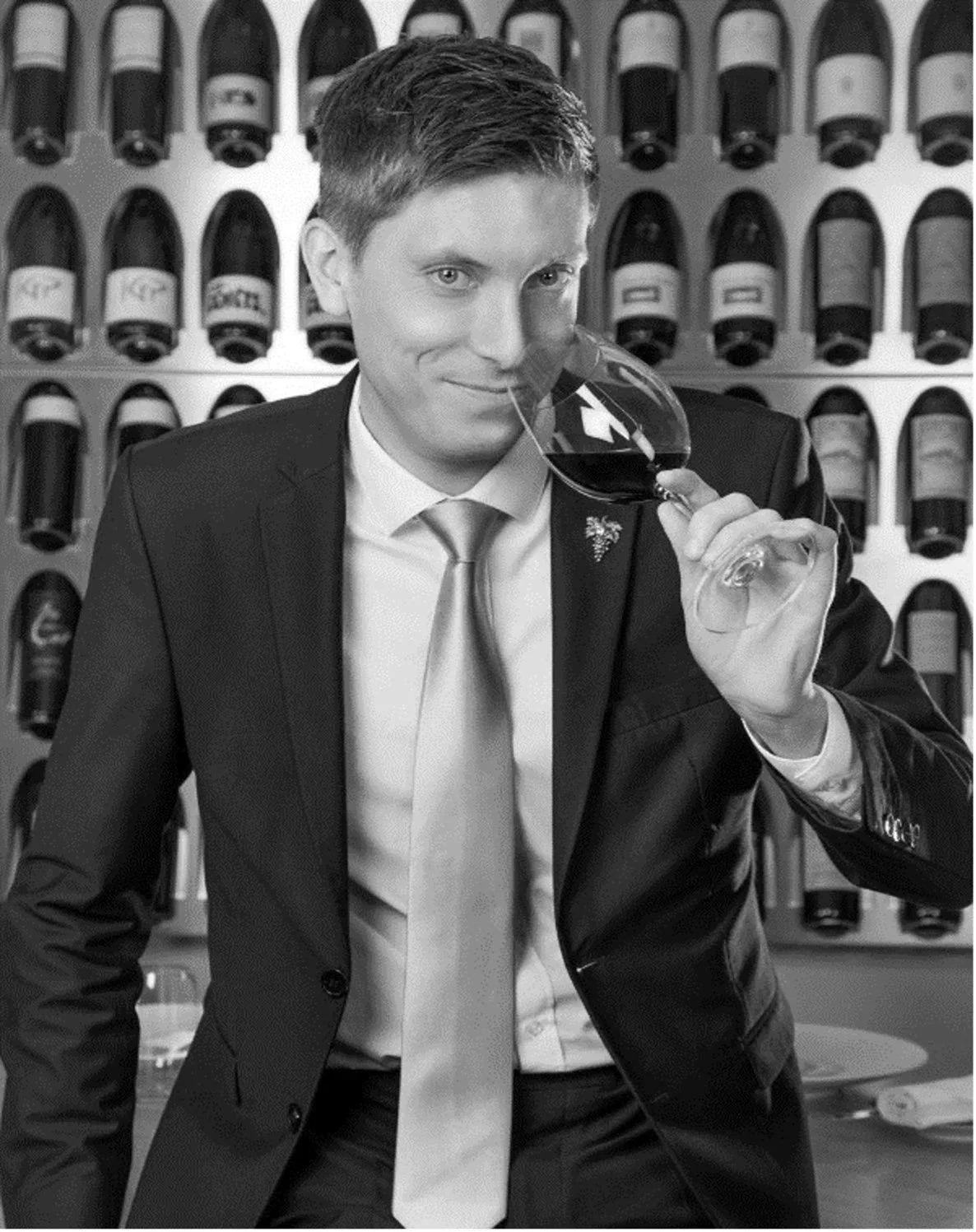 Un homme en costume en train de boire du vin rouge dans un vinothèque.