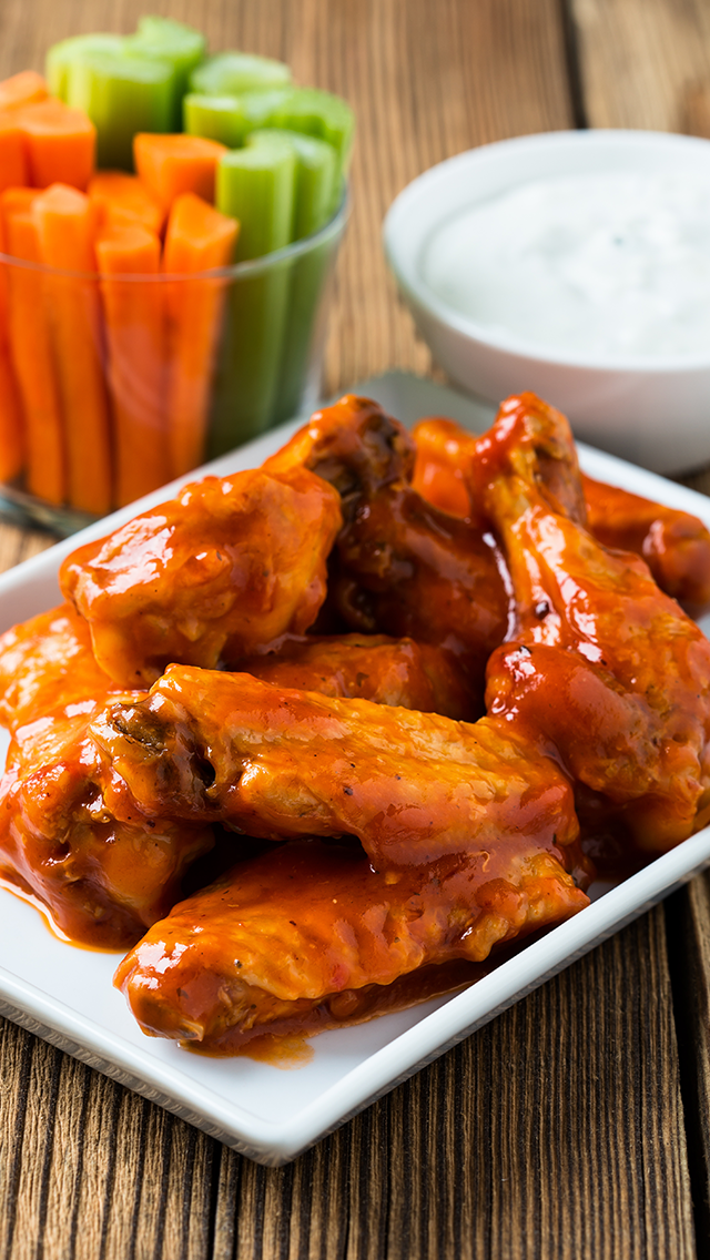 Buffalo chicken wings coated in sauce with celery sticks and ranch dressing in the background.
