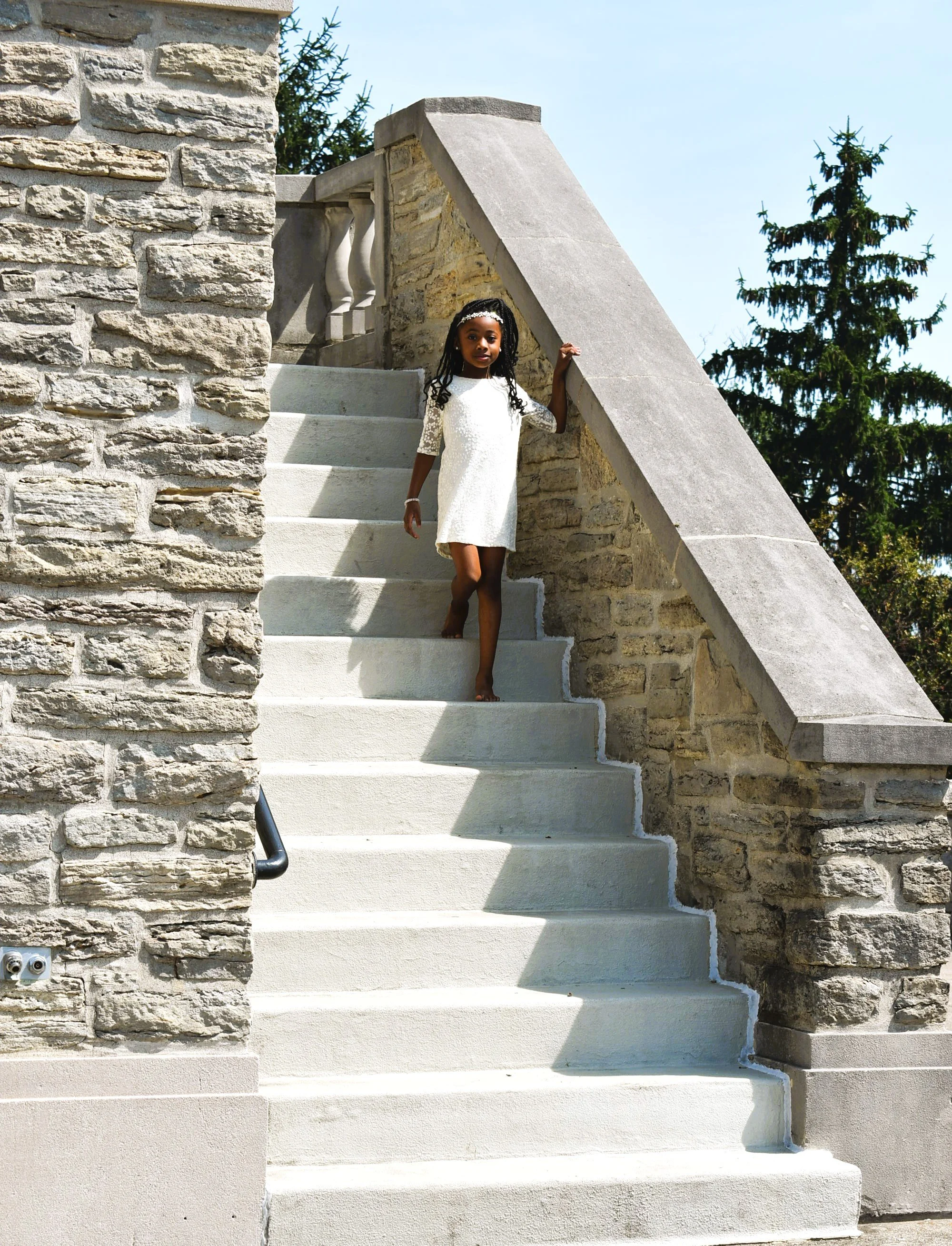 A young girl in a white dress walking down outdoor stone stairs.