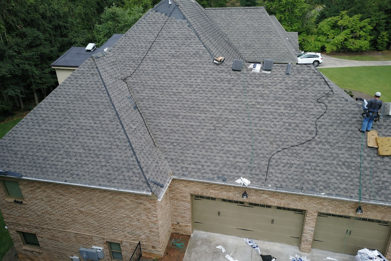 An aerial view of a house roof with a worker in safety gear cleaning the gutters.