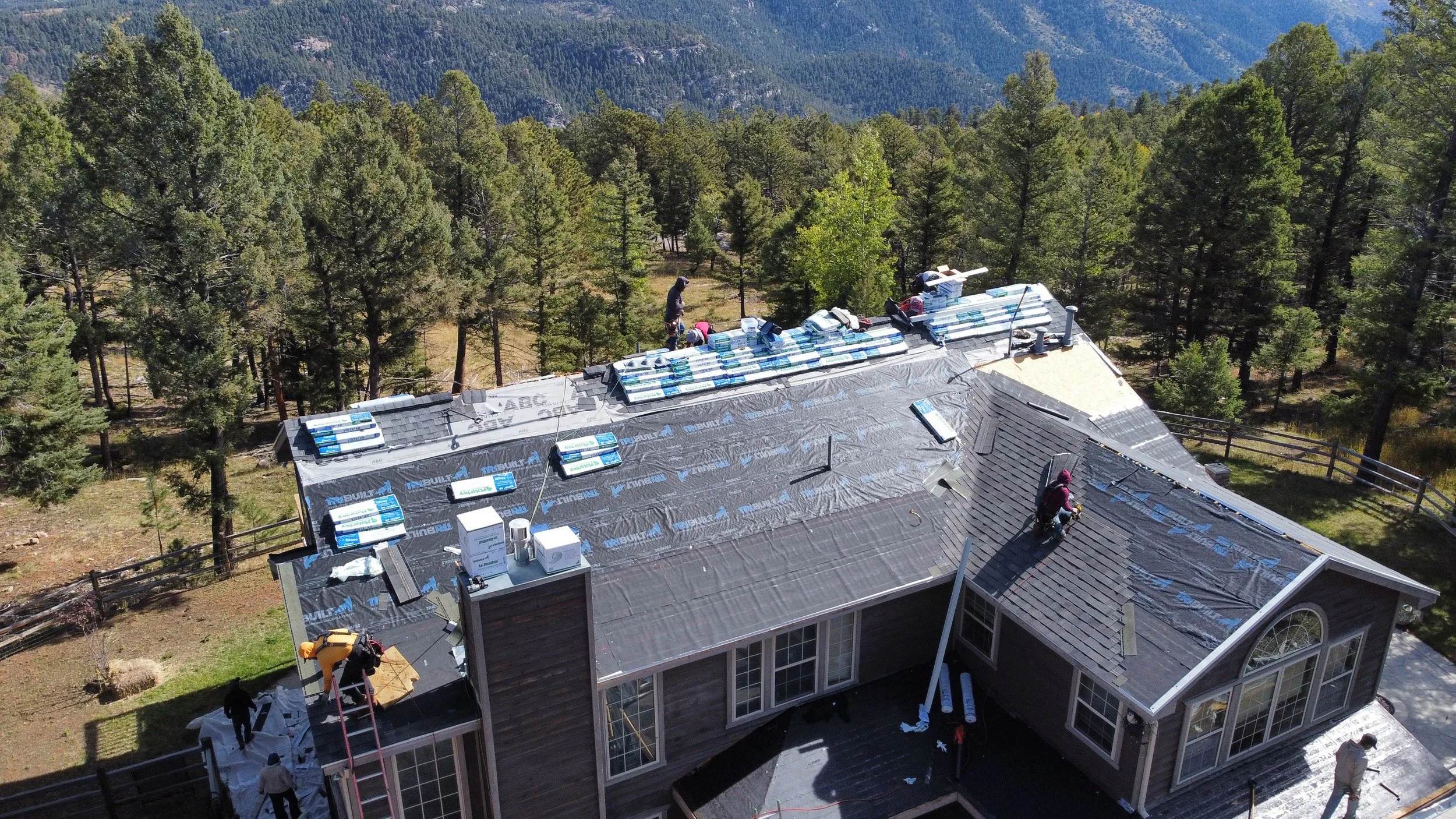 Aerial view of people working on roofing of a house surrounded by trees in a forested area.