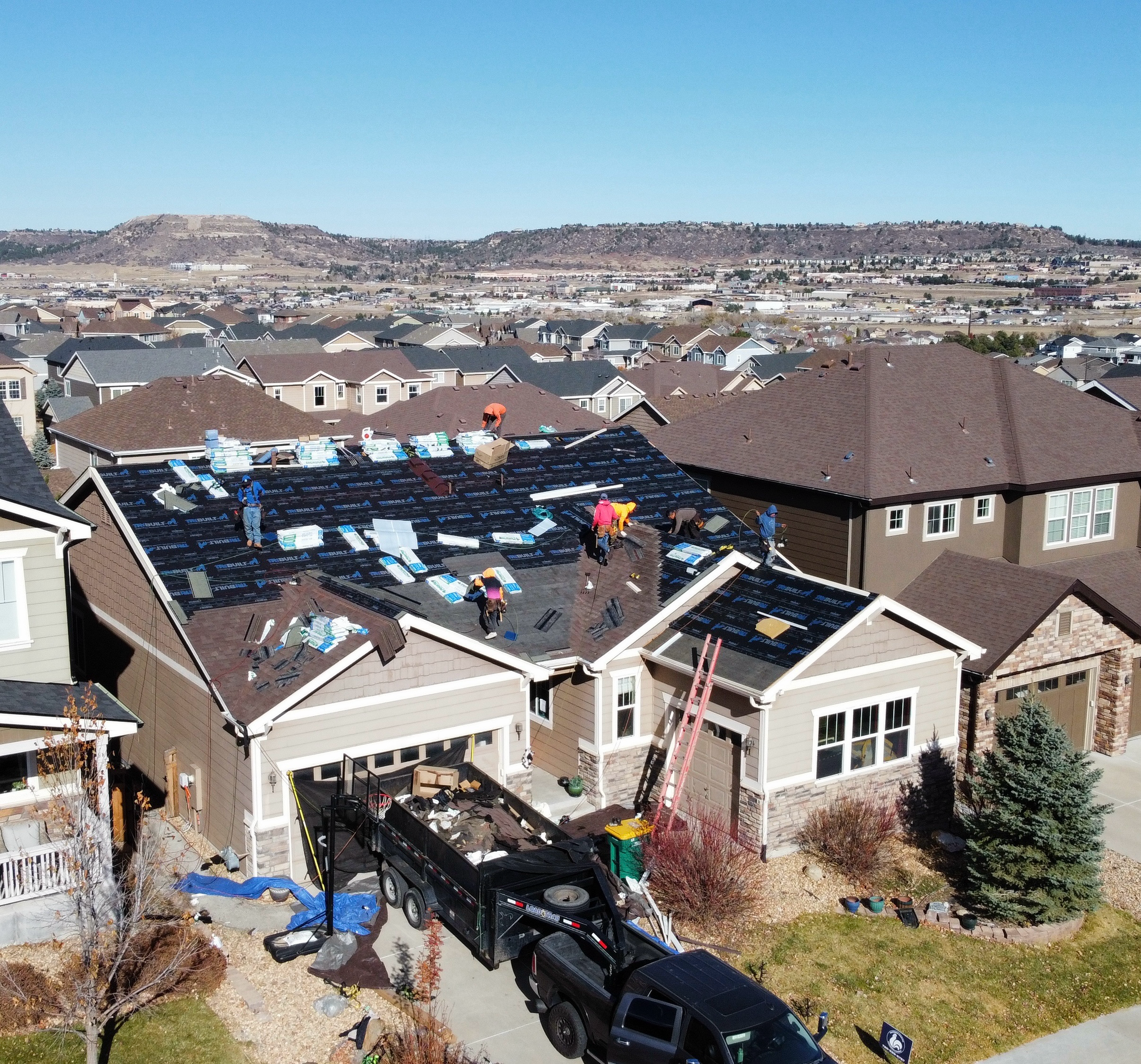 Construction workers installing roofing on a two-story house in a suburban neighborhood.