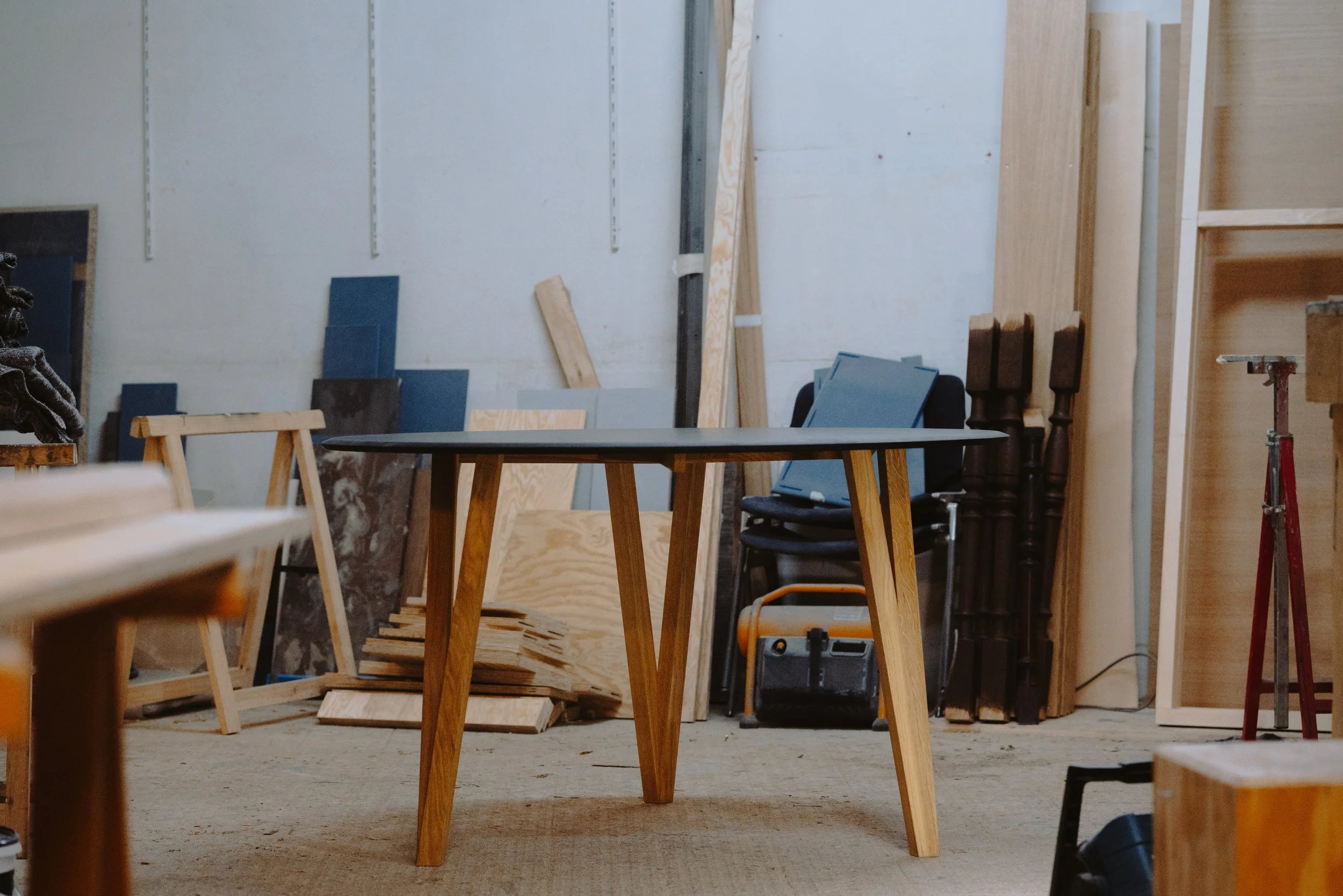 Une pièce en construction avec une table en bois au centre, des planches de bois et des matériaux de construction disposés autour, murs en fond en cours d'aménagement.