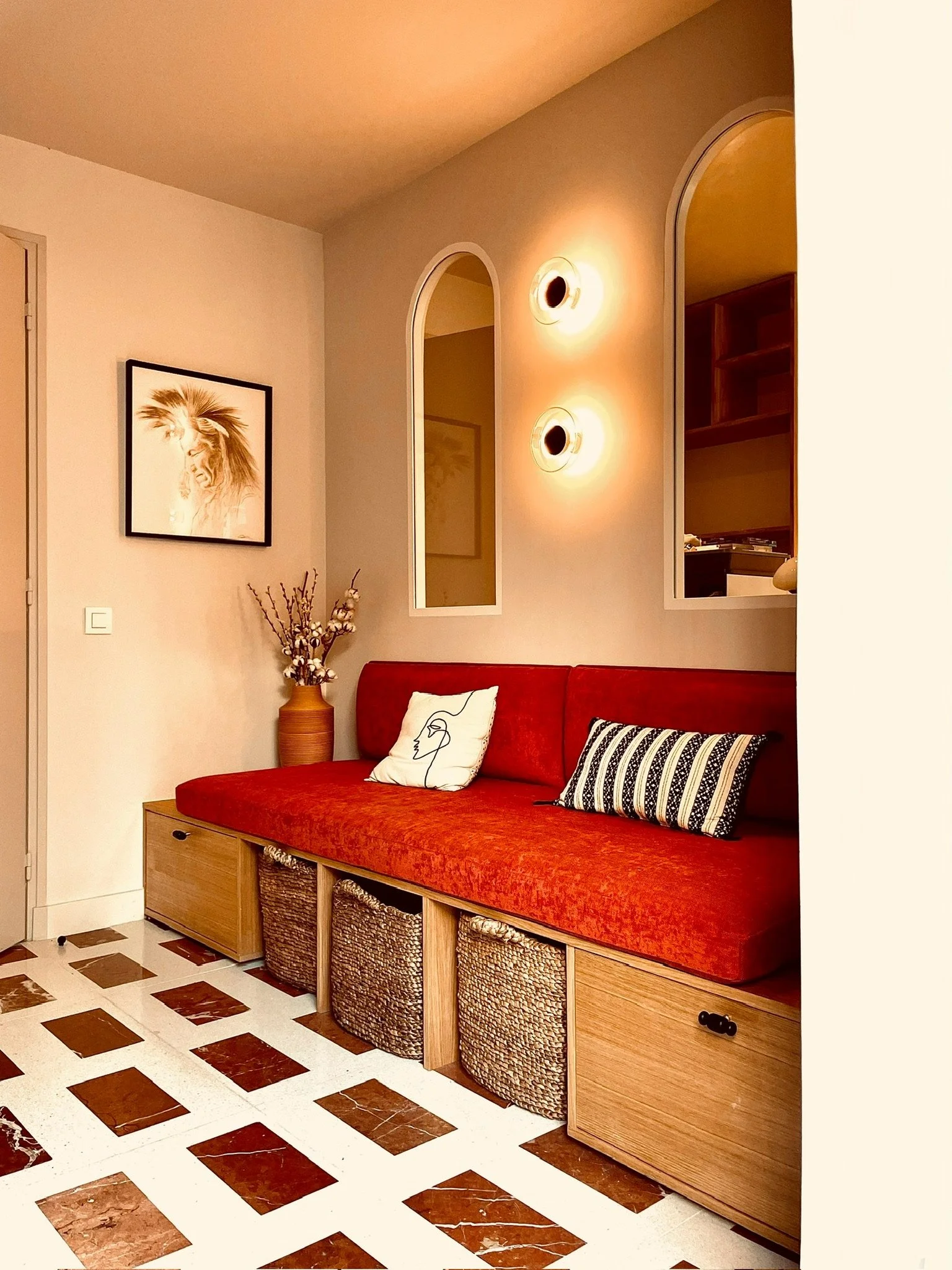 Salon avec un canapé rouge, une décoration florale, une peinture de lion au mur, et un éclairage mural.