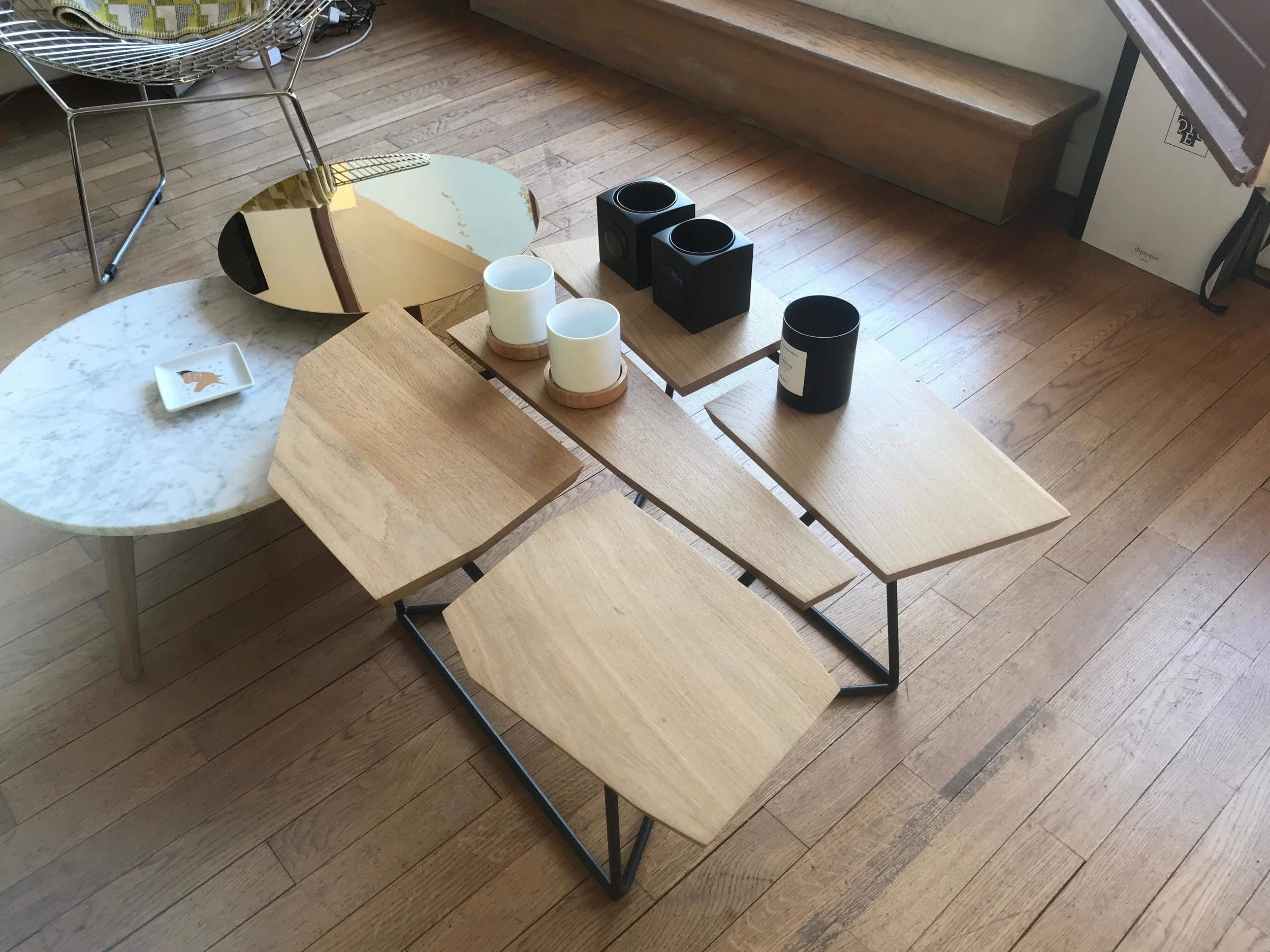 Table basse en bois avec plusieurs plateaux rectangulaires en bois clair, some are above a black metal structure, et d'autres en dessous, disposée dans une pièce avec plancher en bois.