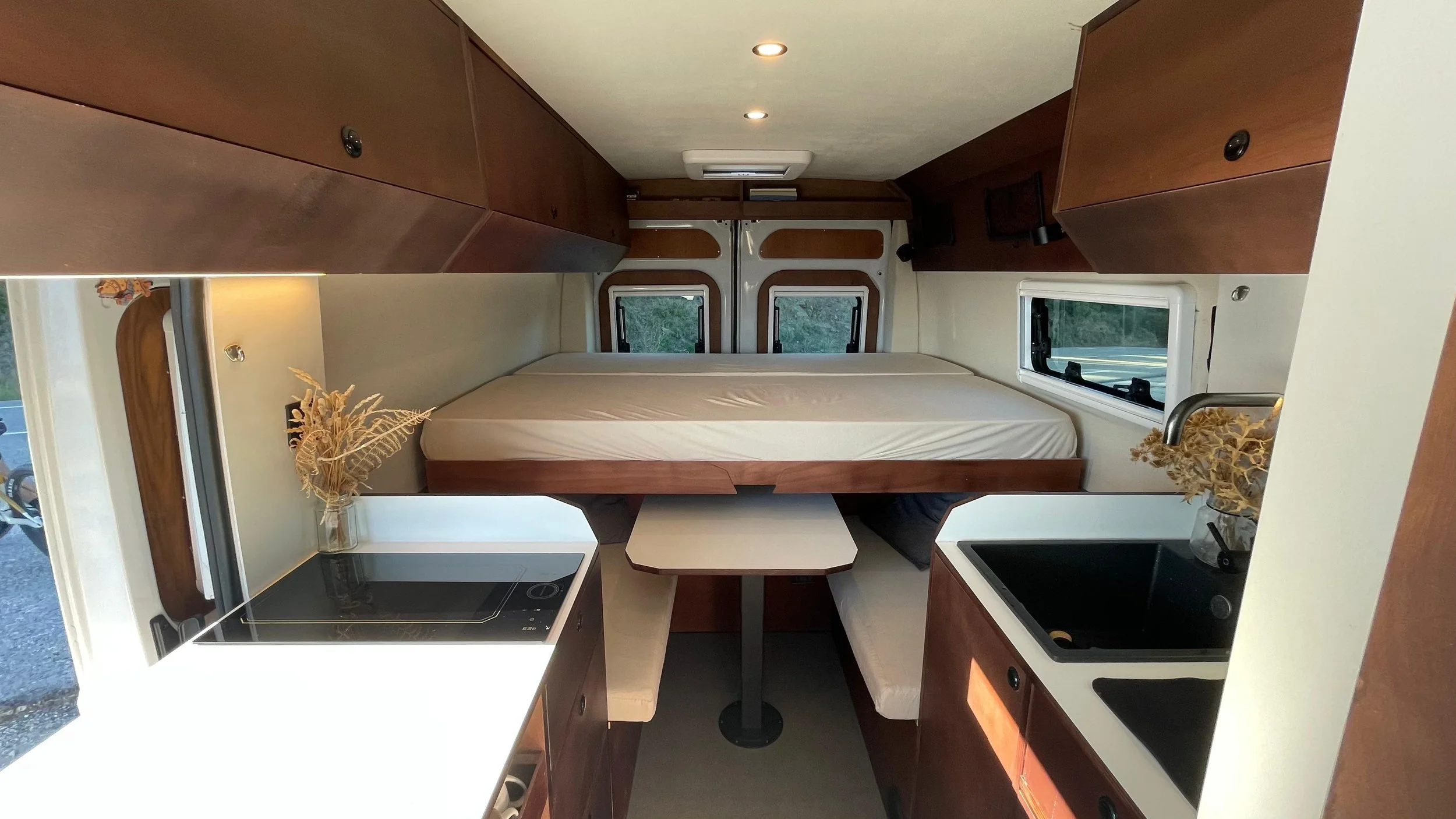 Intérieur d'un camping-car ou d'une petite maison mobile avec une zone de vie comprenant une chambre, une salle à manger, une cuisine et une salle de bain, avec un toit ouvrant visible.