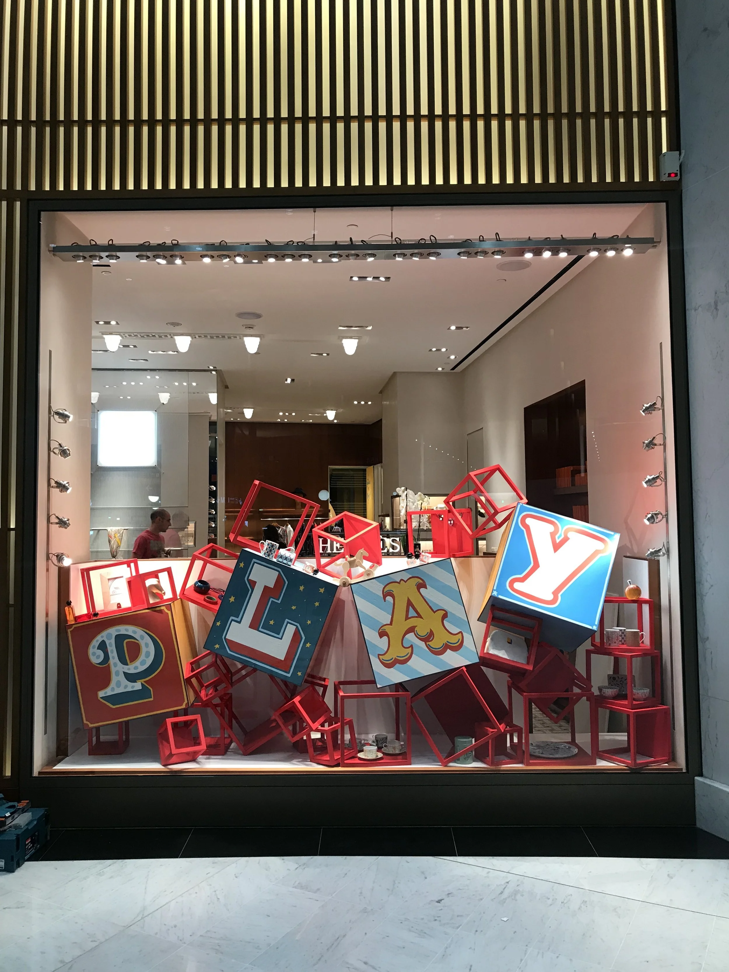 Vitrine d'un magasin avec décoration colorée comprenant des blocs et lampes, probablement une vitrine de fête ou de décoration, avec des lettres formant 'PLAY' dans des cubes colorés.