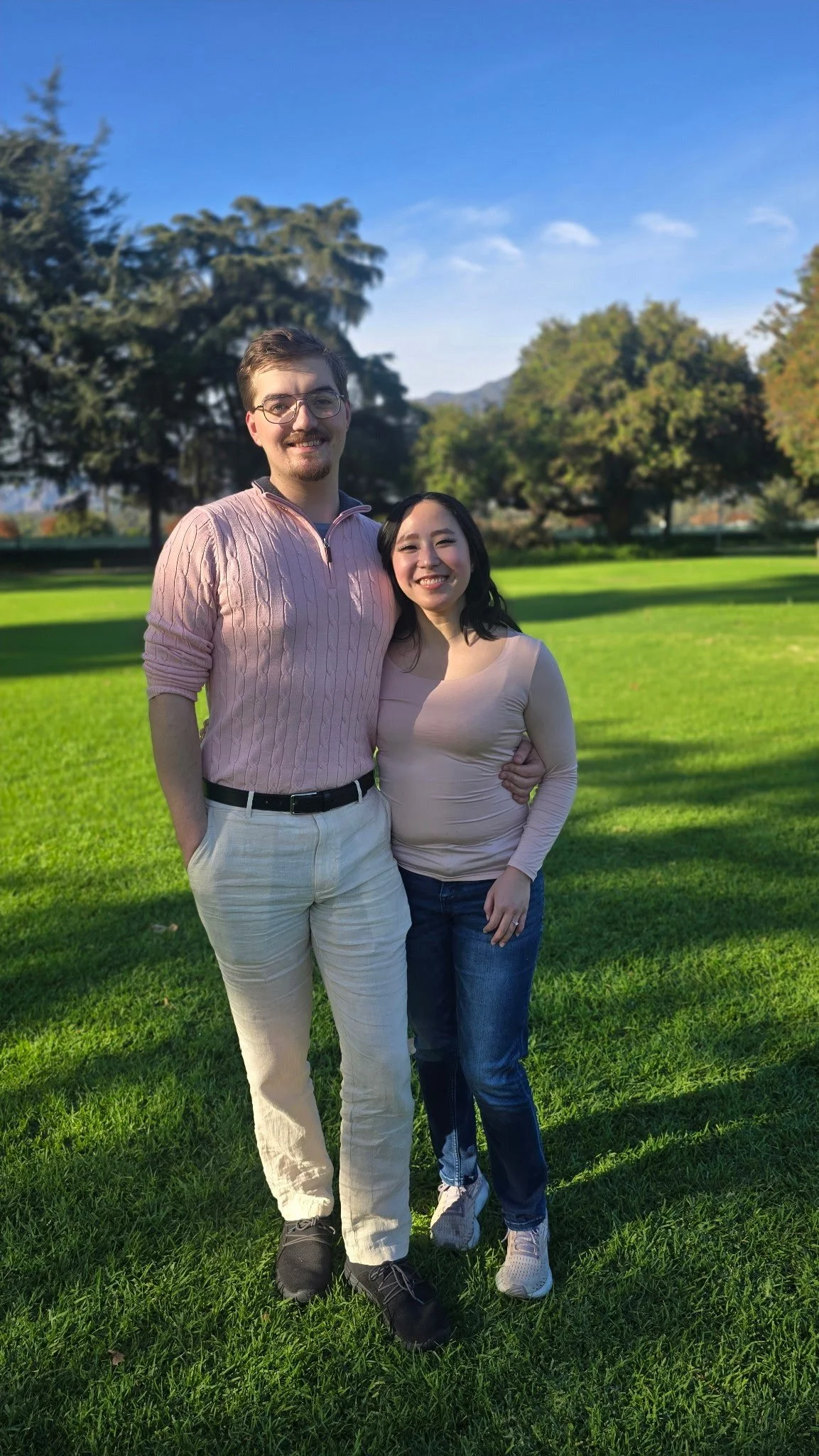 A photo of Lesley and Kyle in a park. Lesley and Kyle are wearing pink sweaters.