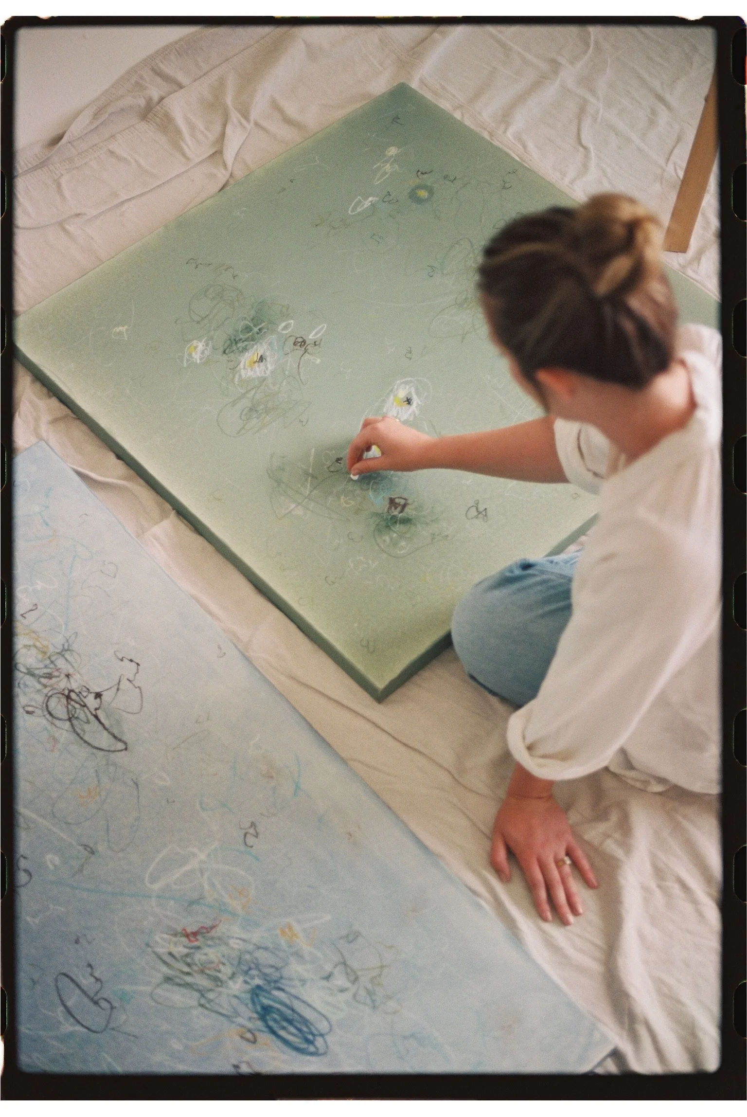 A person drawing on a large piece of glass with colorful markers, surrounded by scribbles and doodles.