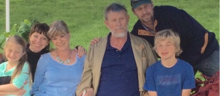 Group of five people, including two children and three adults, standing outdoors on a grassy area.