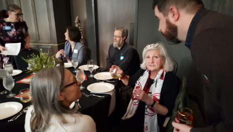 A group of people gathered around a dinner table in a restaurant, engaging in conversation and sharing drinks.