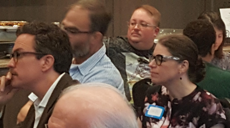 A diverse group of people sitting and listening at an indoor event or conference.