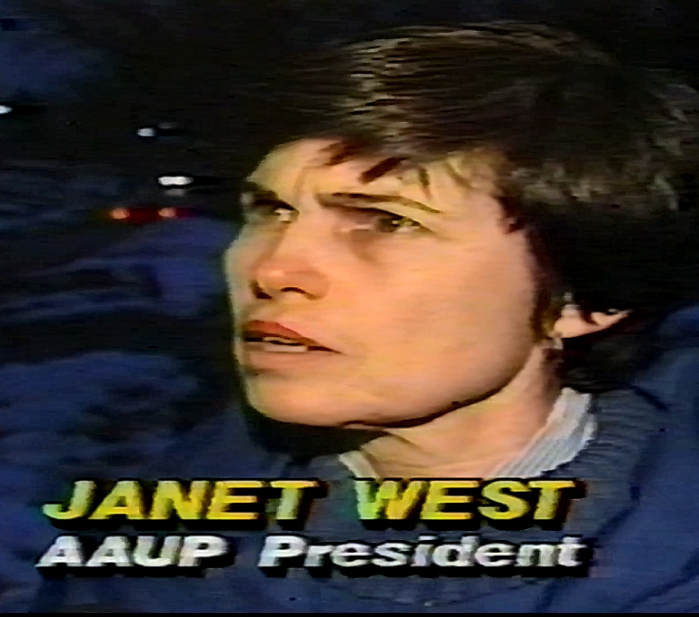 A woman with dark hair and a serious expression, wearing a blue jacket, in what appears to be a news interview or broadcast. Text on the image reads 'Janet West, AAUP President.'