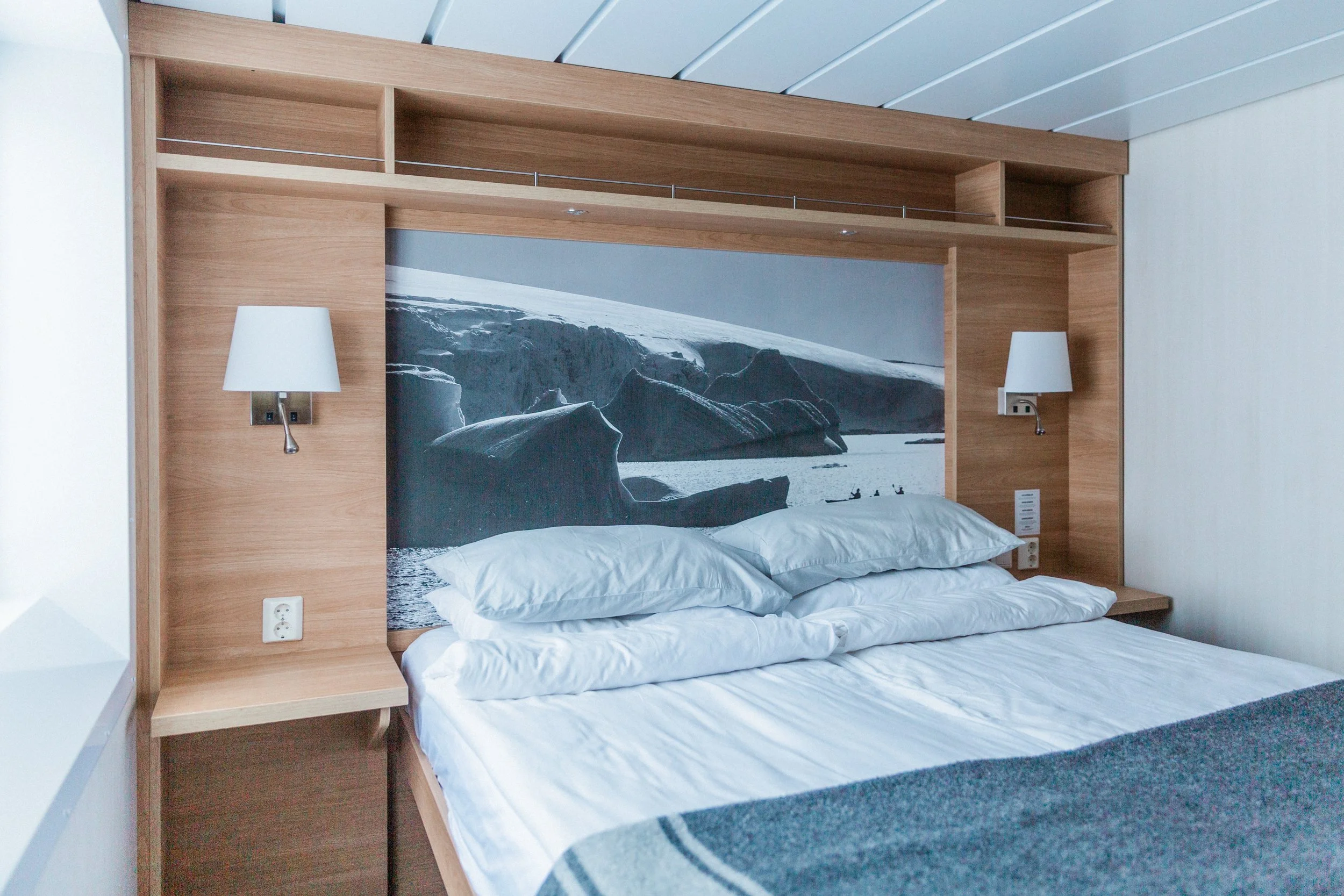 Arctic Superior cabin with a double bed, pale wood headboard, built‑in shelves and a large black‑and‑white glacier photograph above the bed.