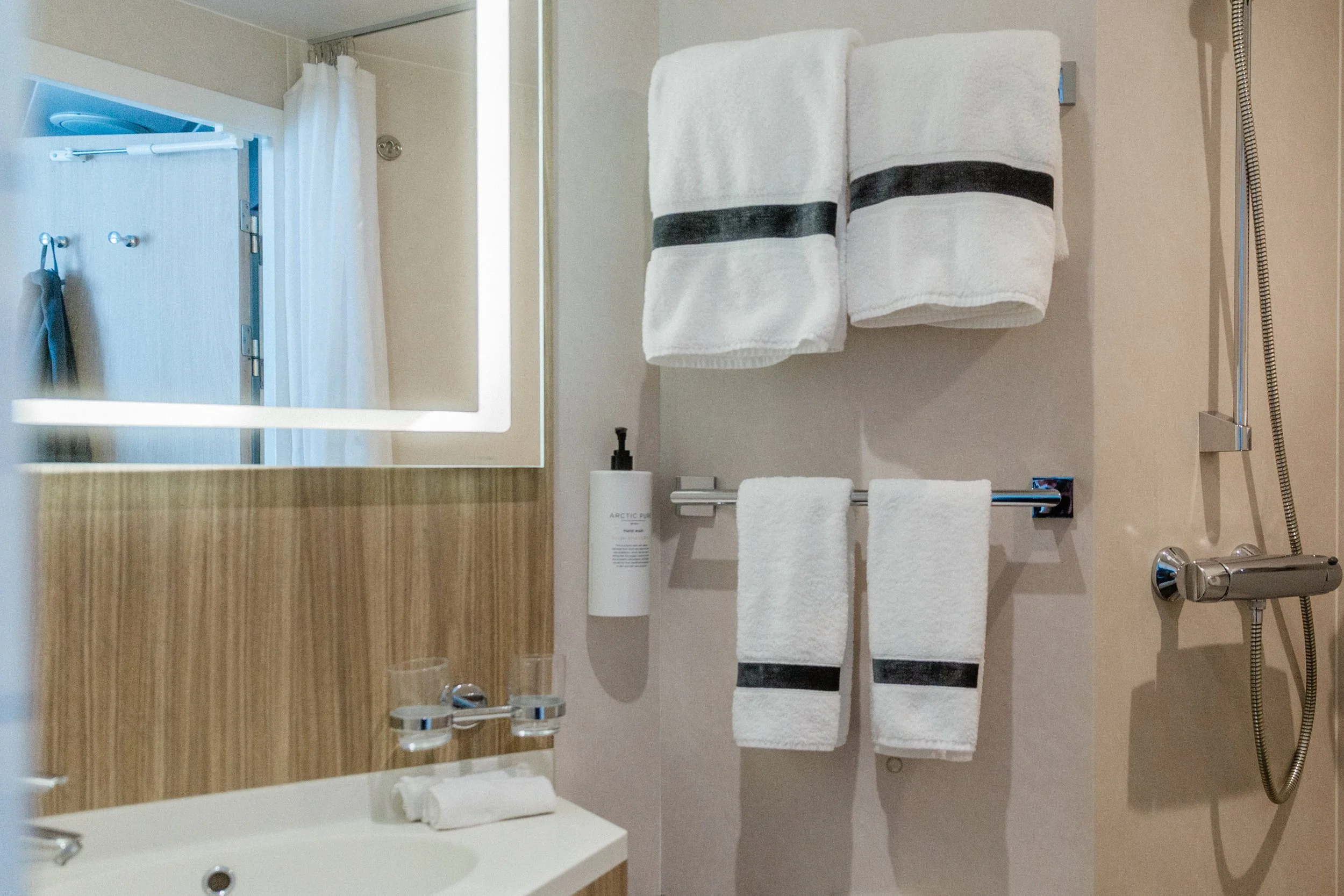 Modern Arctic Superior bathroom with a lighted mirror, white towels, a sink with glasses, and a chrome shower fixture.
